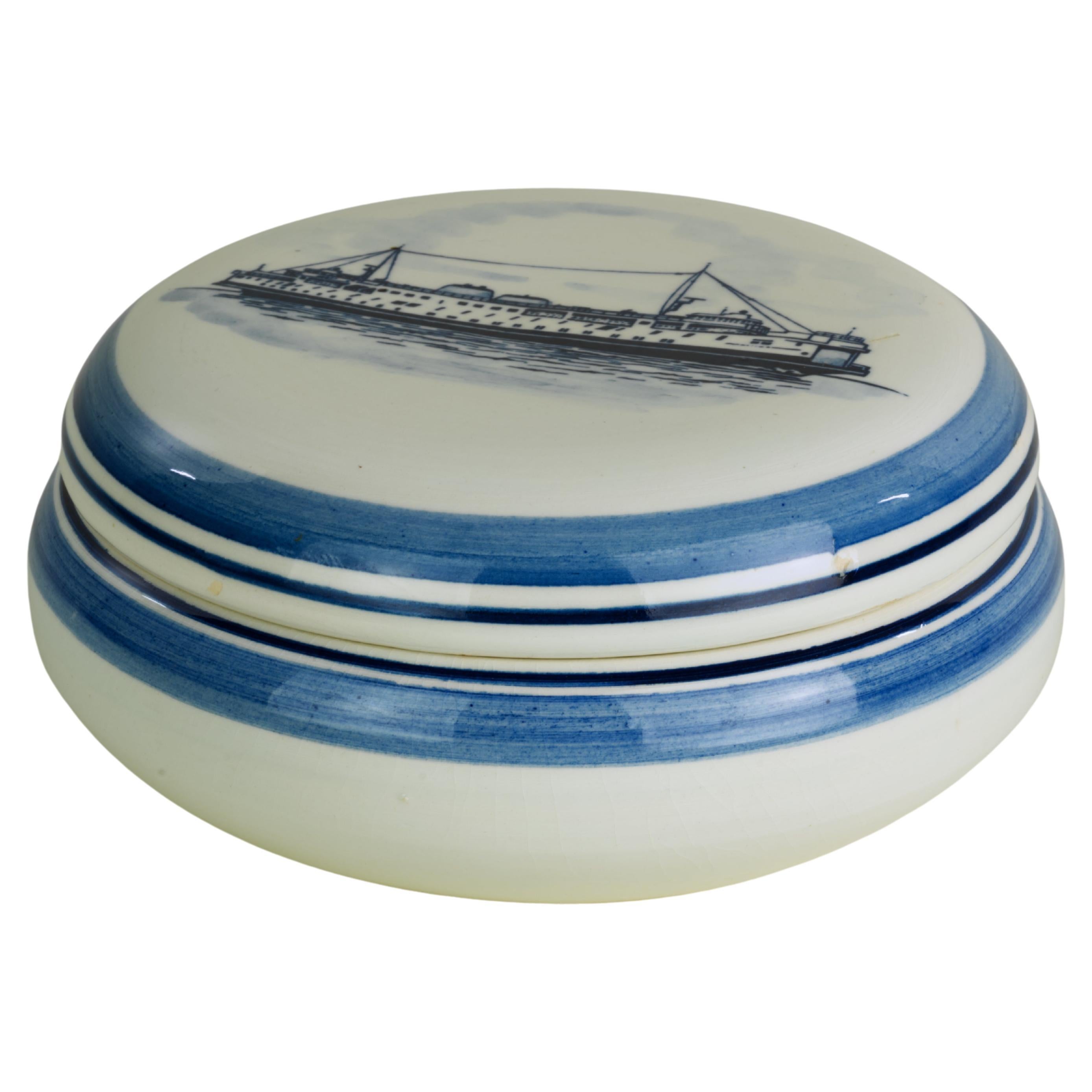 
Vintage promotional advertising jar with lid is made of glazed ceramics and is decorated with two-tone blue drawing of a ship on a sea. It is marked in blue script on the inner side if the lid. The marks include company logo, company name, Jan