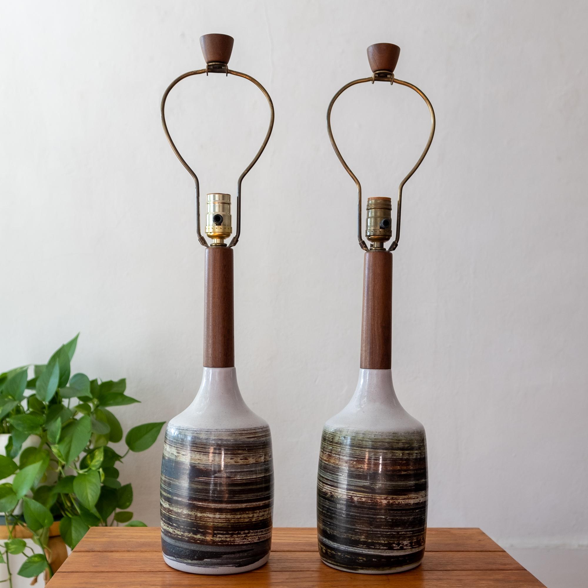 A pair of ceramic and turned walnut lamps by Jane and Gordon Martz for their company, Marshall Studios. Natural tan clay, brushed linear glaze design around the entire base. Includes original harps and finials. Signed.