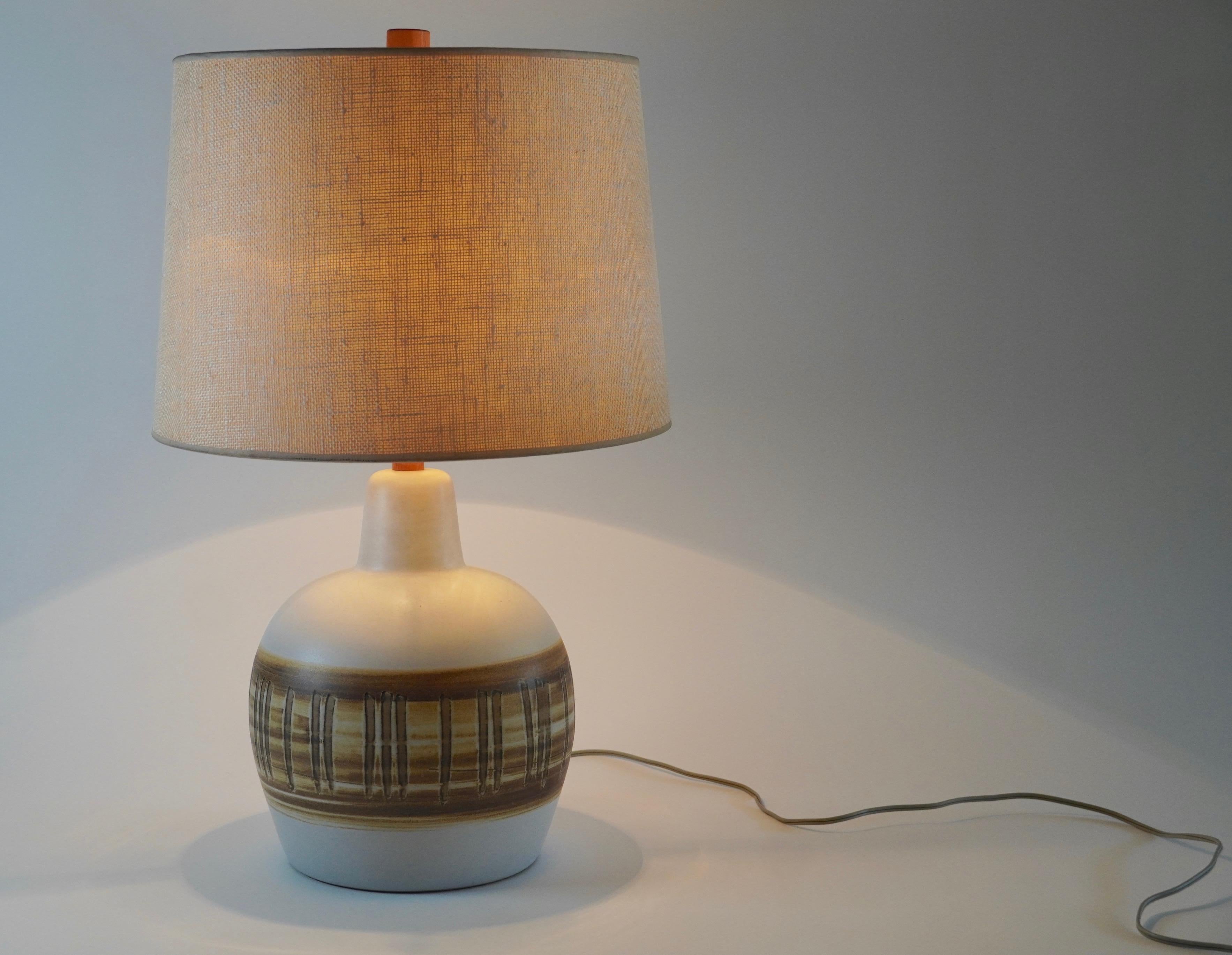 All original Martz ceramic table lamp with shade having beige and brown hand painted glazes with both vertical and horizontal design patterns across the center of the lamp resting on a walnut base designed by Jane & Gordon Martz and produced by