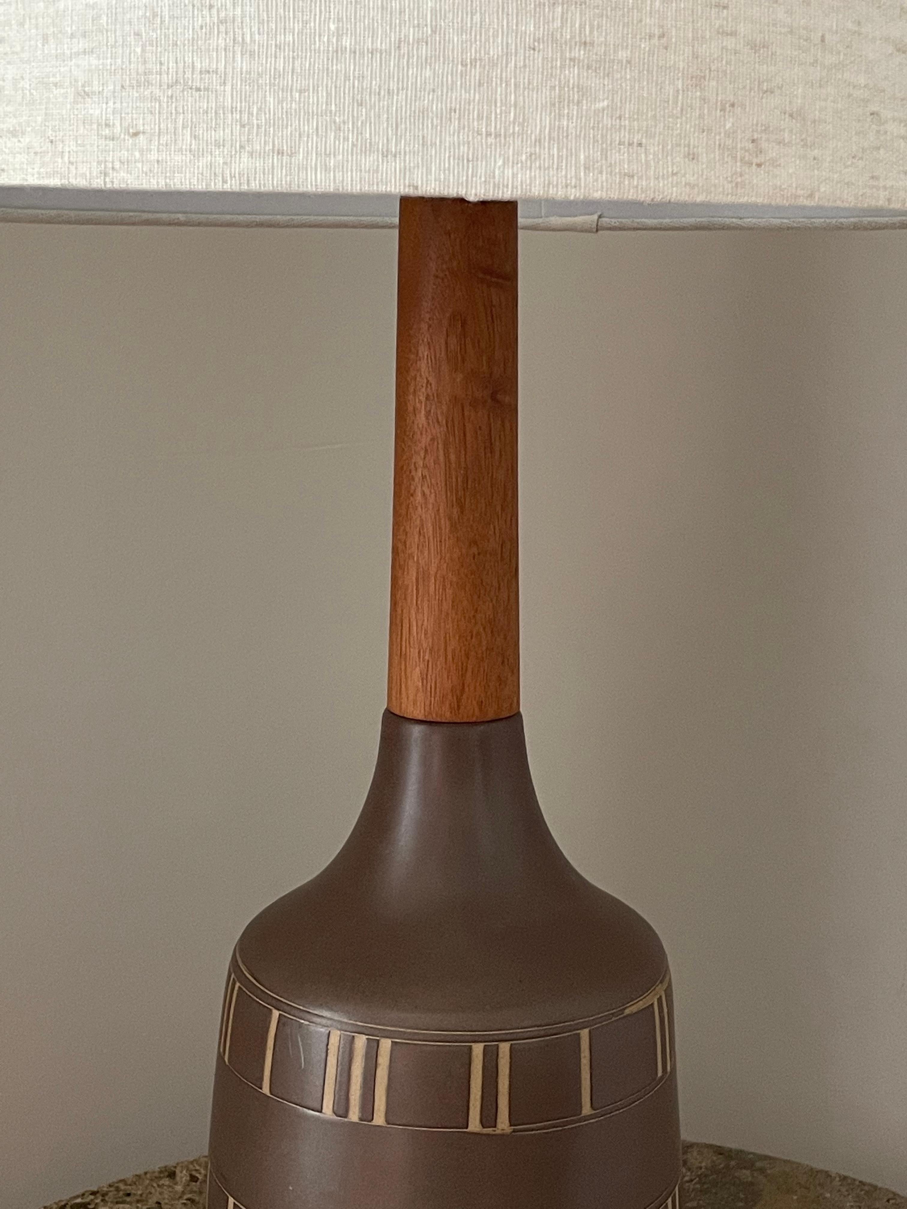 Magnifique lampe de table haute conçue par le célèbre duo de céramistes Jane et Gordon Martz pour Marshall Studios. La glaçure est d'un brun foncé mat et le motif est incisé. Long col en noyer avec embout de finition en noyer.

Dimensions globales