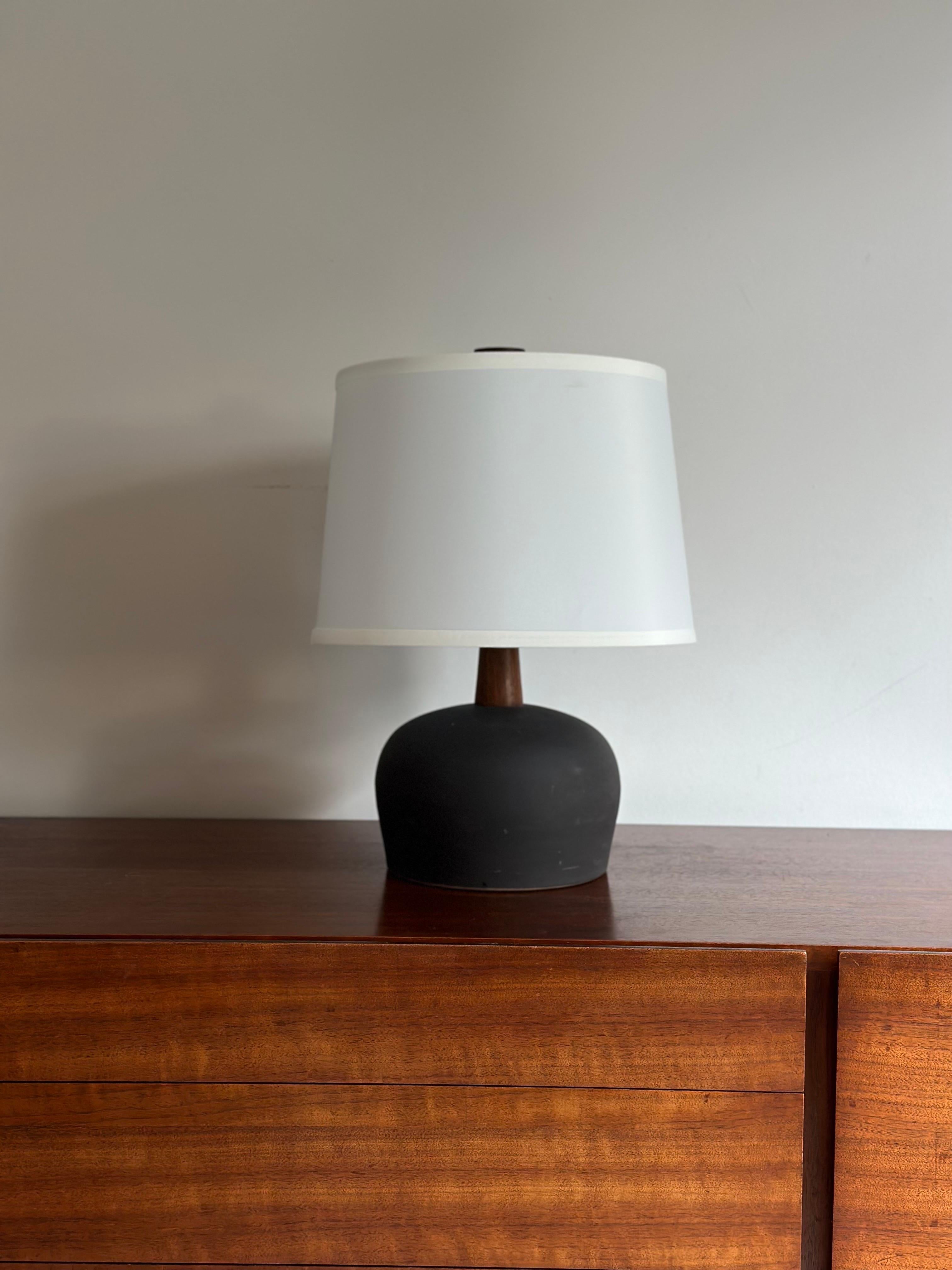 Table lamp designed by famed ceramicist duo Jane and Gordon Martz for Marshall Studios. Ceramic base with walnut neck and finial. Great rough matte black glaze.

Dimensions:
Overall
18” tall
13” wide

Ceramic Portion
5..75” tall
8” wide

Shade shown