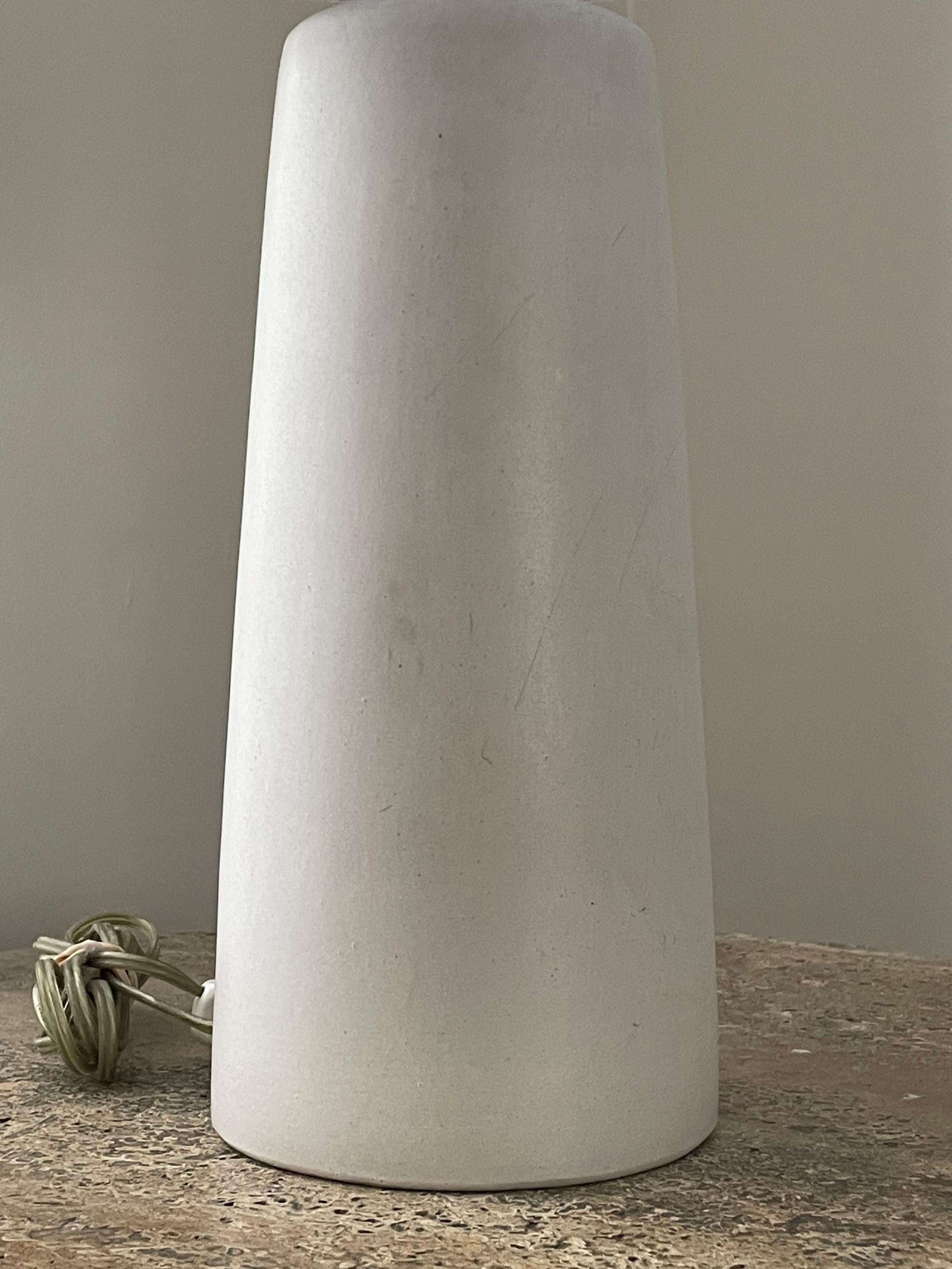 Wonderful minimalist table lamp in ceramic by famed ceramicist duo Jane and Gordon Martz for Marshall Studios. Color is an off white/ faint light grey in a darker setting.

Dimensions:
24” tall
15” wide

Ceramic 
11.5” tall
5.25” wide.

Shade is