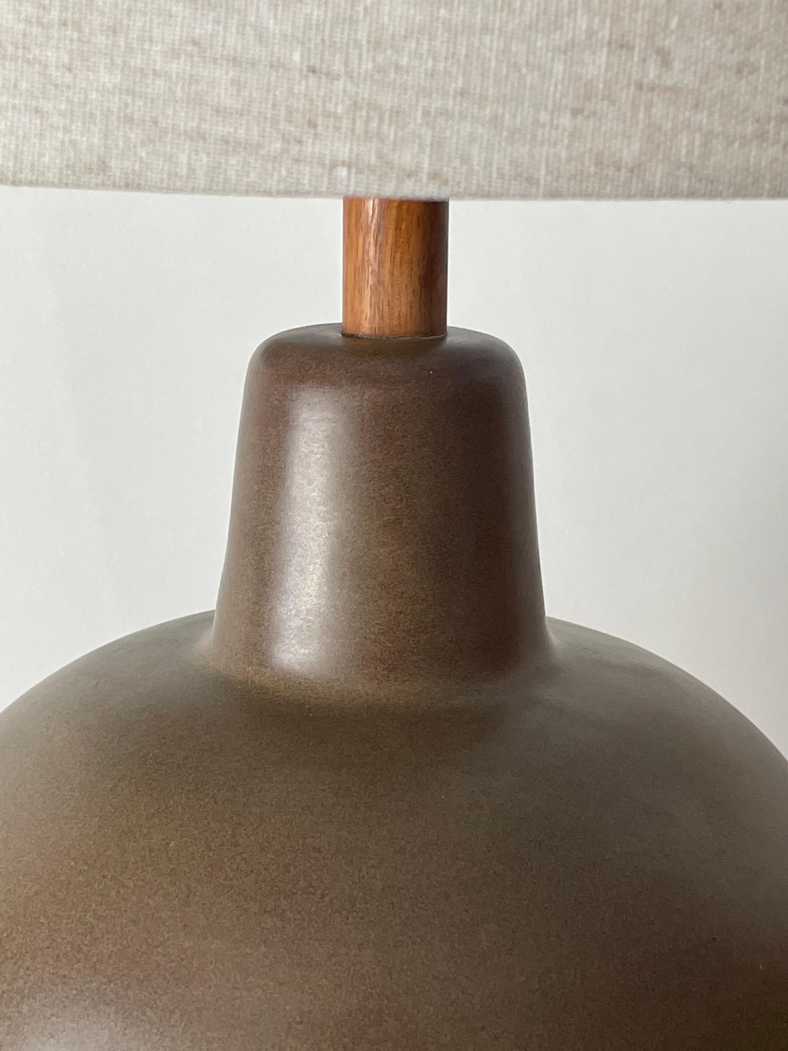 Iconic table lamp by famed ceramicist duo Jane and Gordon Martz for Marshall Studios. Large bulbous form in a matte olive green with subtle dark brown/ purple hue. Great organic color, complimented with original walnut neck and finial.