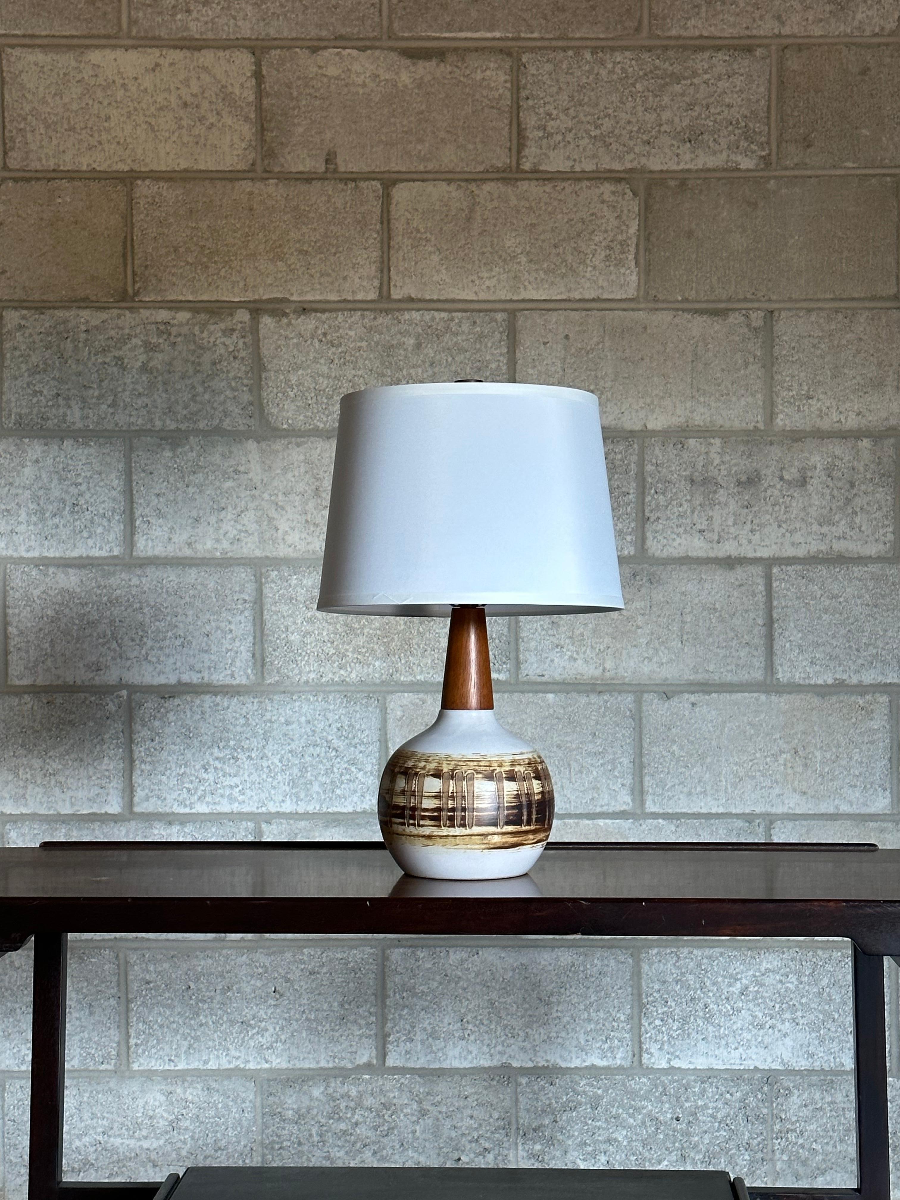 Table lamp designed by Jane and Gordon Martz for Marshall Studios. Featuring a bulbous ceramic body, accented with a long walnut neck, and finished with a walnut finial. A primarily white body with hues of yellow, tan, and brown. 

Overall