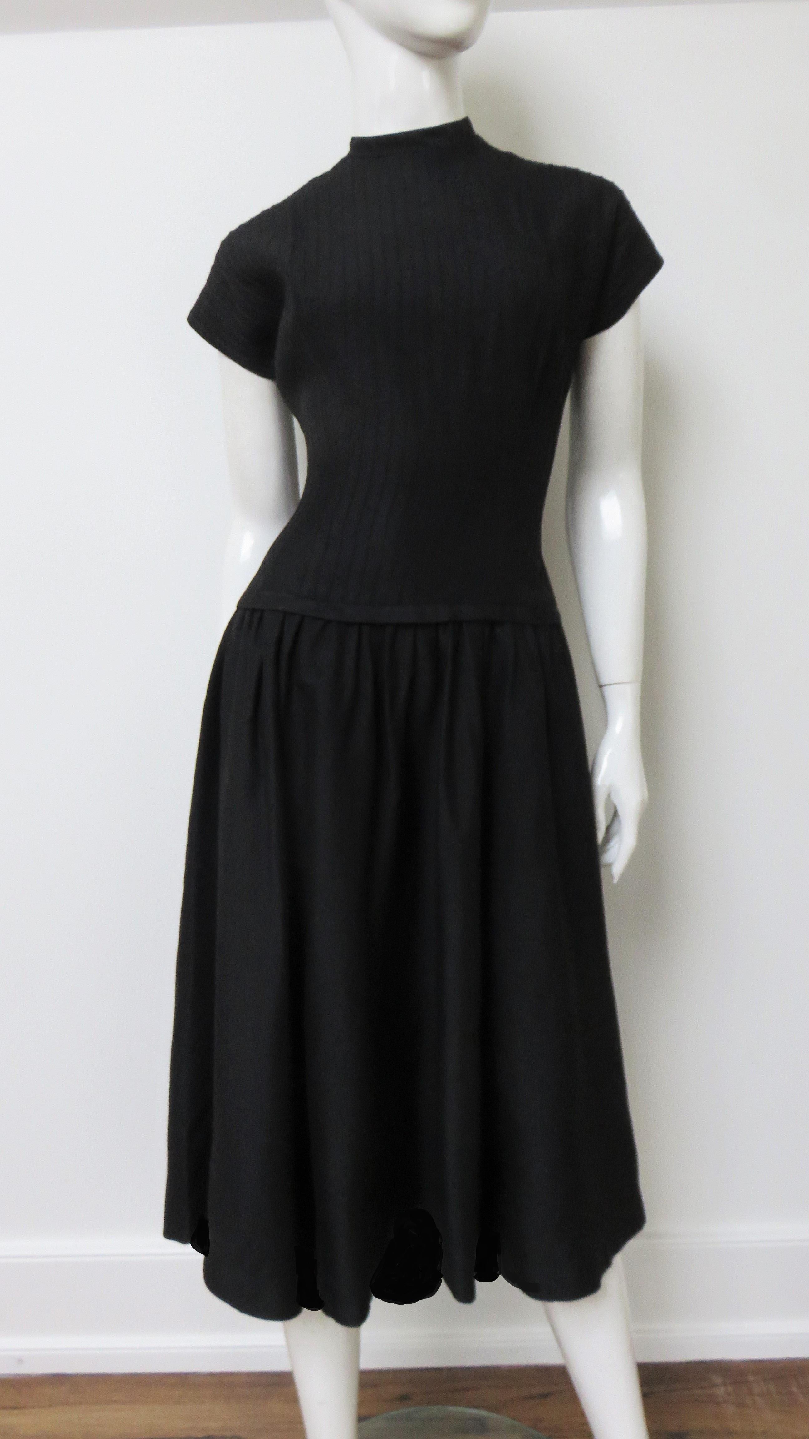 A great black dress by Jane Andre in a cotton linen blend. It has cap sleeves, a drop waist and full skirt. There is fine band around the crew neckline and the drop waistline ending in a small bow at the back of each. The bodice is finely ribbed and