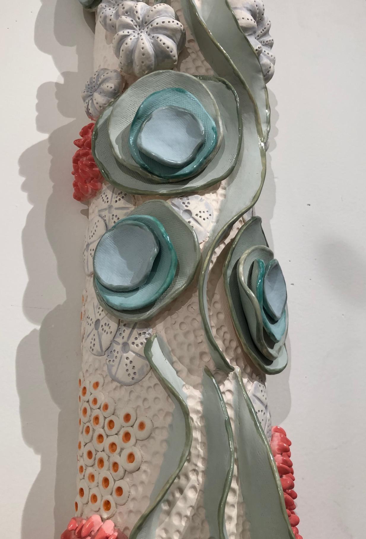 Scultura da parete in ceramica a tema oceanico ispirata alla barriera corallina, pulita, minimale, bianca con verde, rosa corallo, blu pallido e arancione. L'opera è composta da tre parti, ognuna delle quali è appesa a un filo collegato a un chiodo