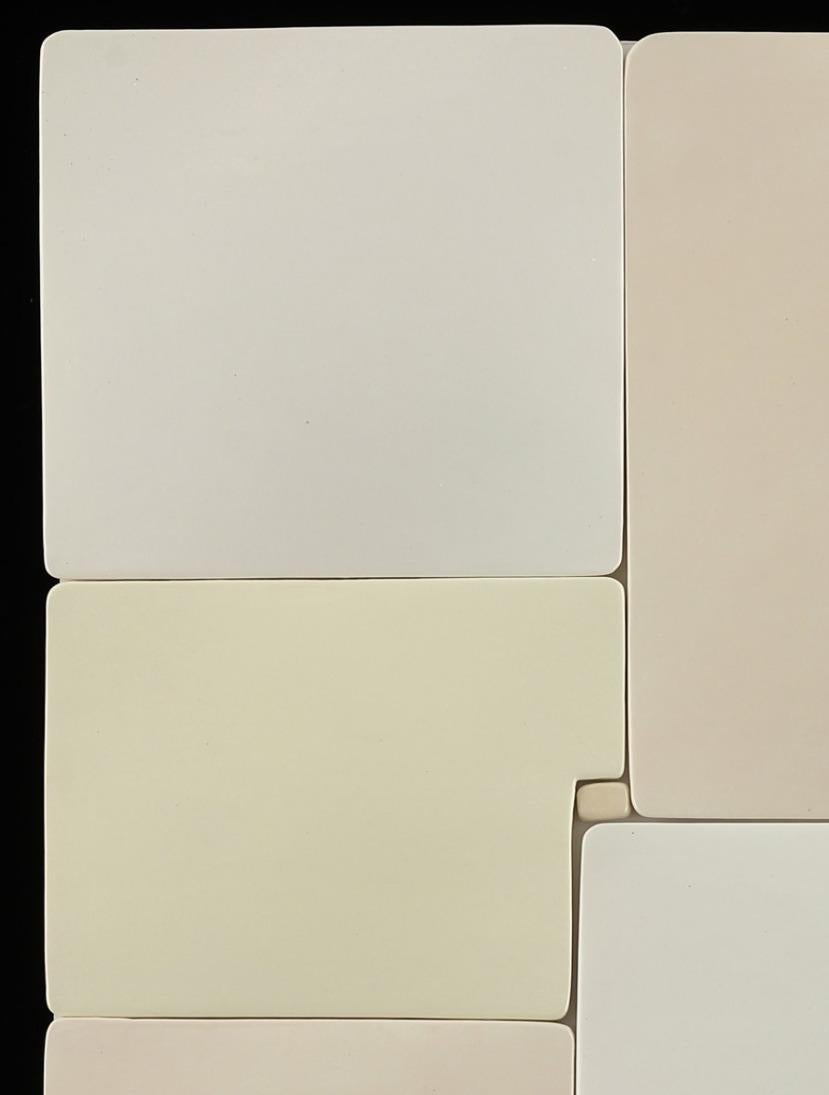 Abstrakte Keramik-Wandskulptur in weiß mit elfenbein/gelb/beige. Ein neutrales Werk aus Keramikquadraten, die auf eine Holzscheibe montiert sind  von der Pop-Art-Pionierin Jane B. Grimm, deren minimalistische und meditative Skulpturen und