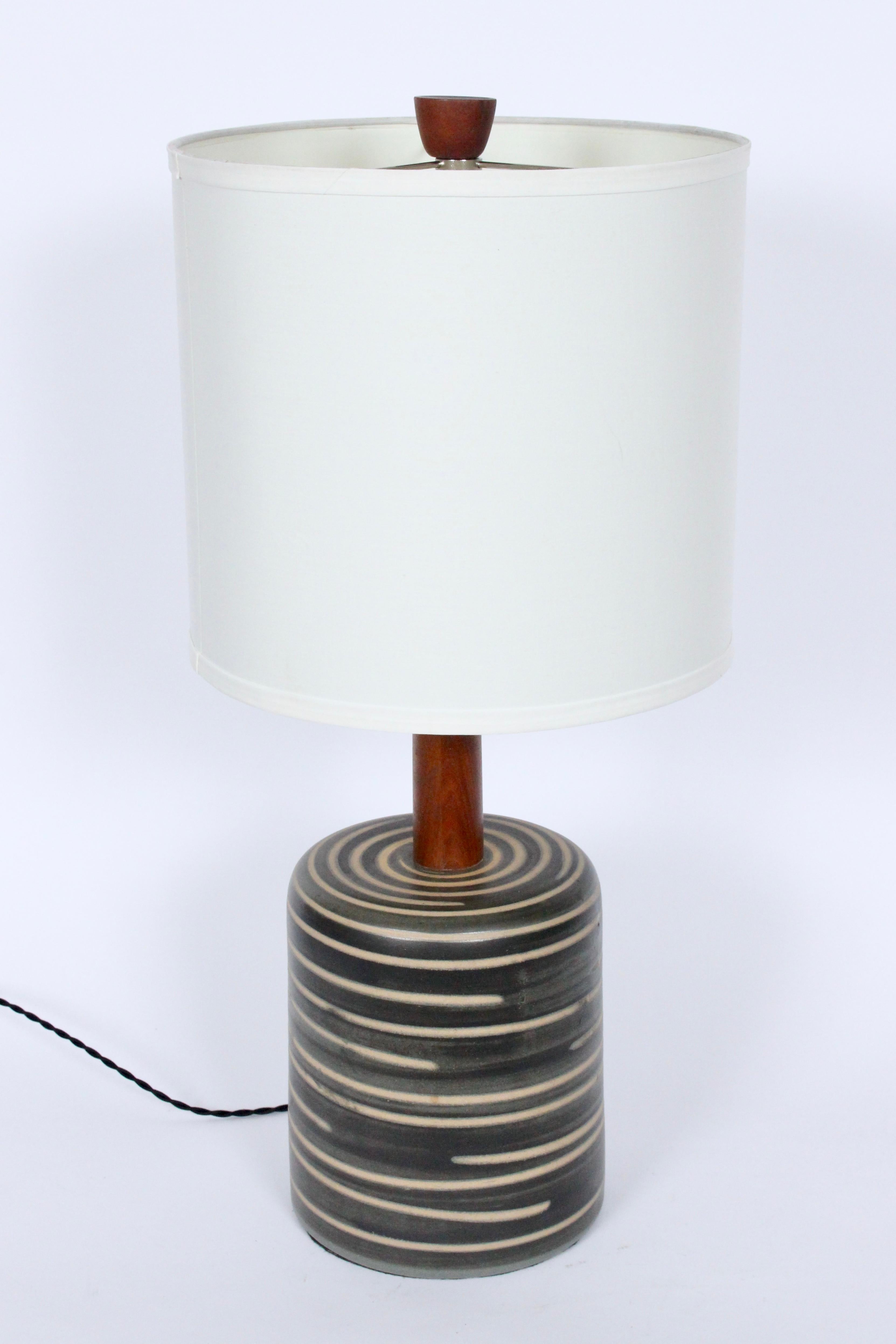 Gordon Martz for Marshall Studios olive and tan M217 table lamp, 1960's. Featuring a matte glazed charcoal, olive green stoneware body with contrasting Beige, Tan banding. Original teak shaft and finial. 18H to socket. Ceramic 9H. Shade shown for