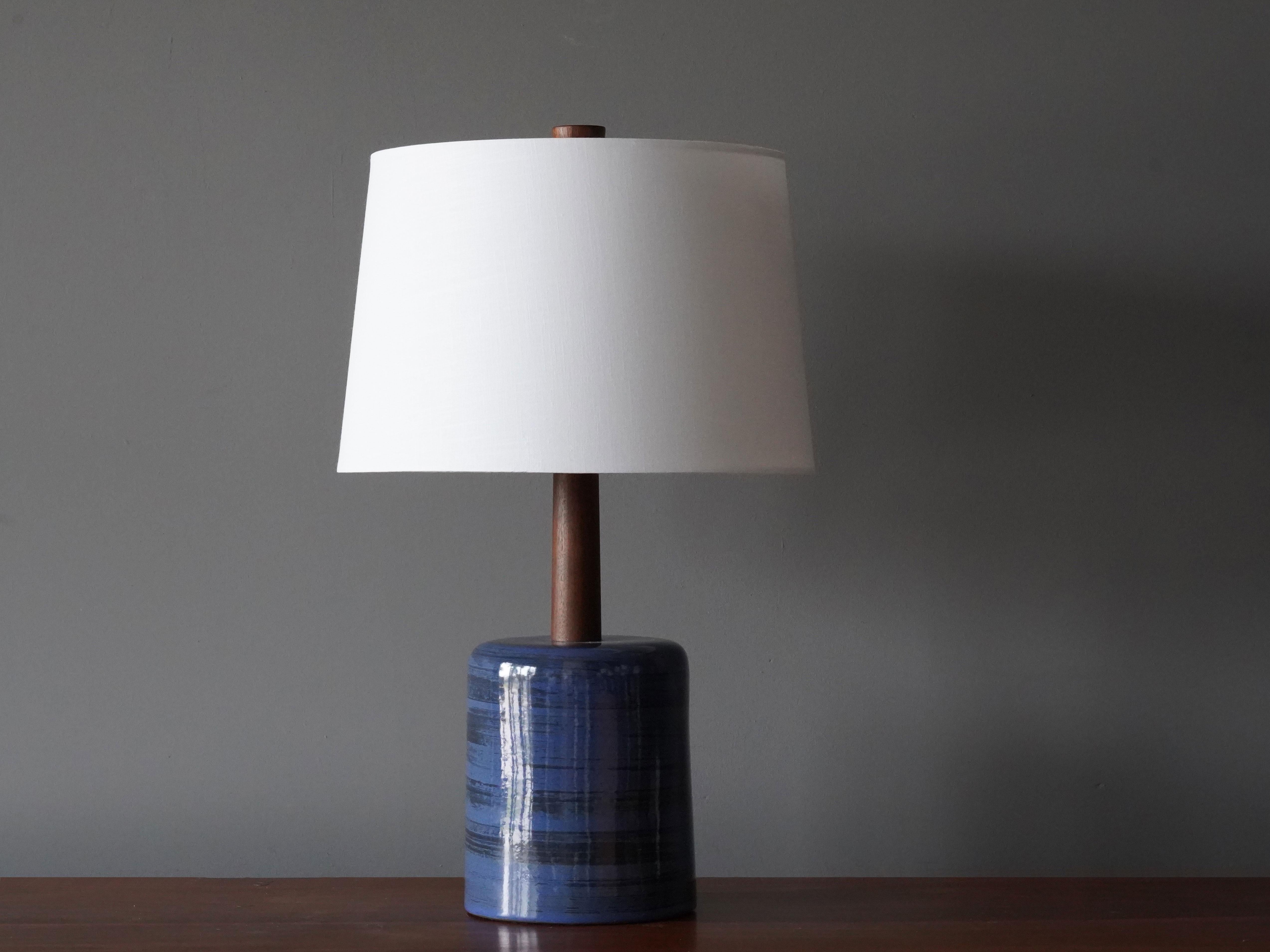 A table lamp designed by husband and wife duo Jane & Gordon Martz. Produced by Marshall Studios, Indianapolis. 

The blue base is slip-cast and then dipped into glaze and hand painted. Design also incorporates exquisite walnut neck and finial. Base