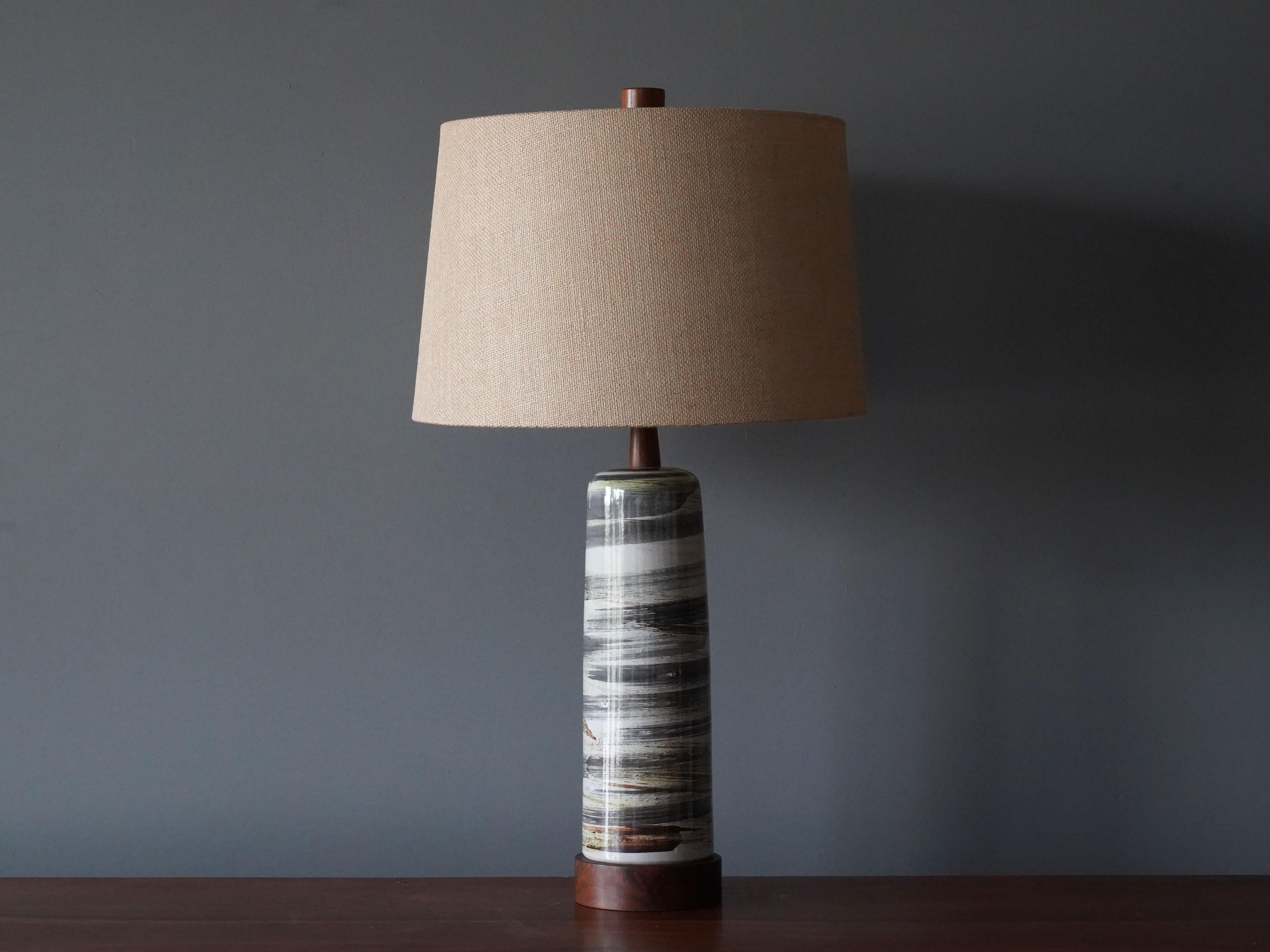 A table lamp designed by husband and wife duo Jane & Gordon Martz. Produced by Marshall Studios, Indianapolis. 

The gray / green base is slip-cast and then dipped into glaze and hand painted. Design also incorporates exquisite walnut neck and