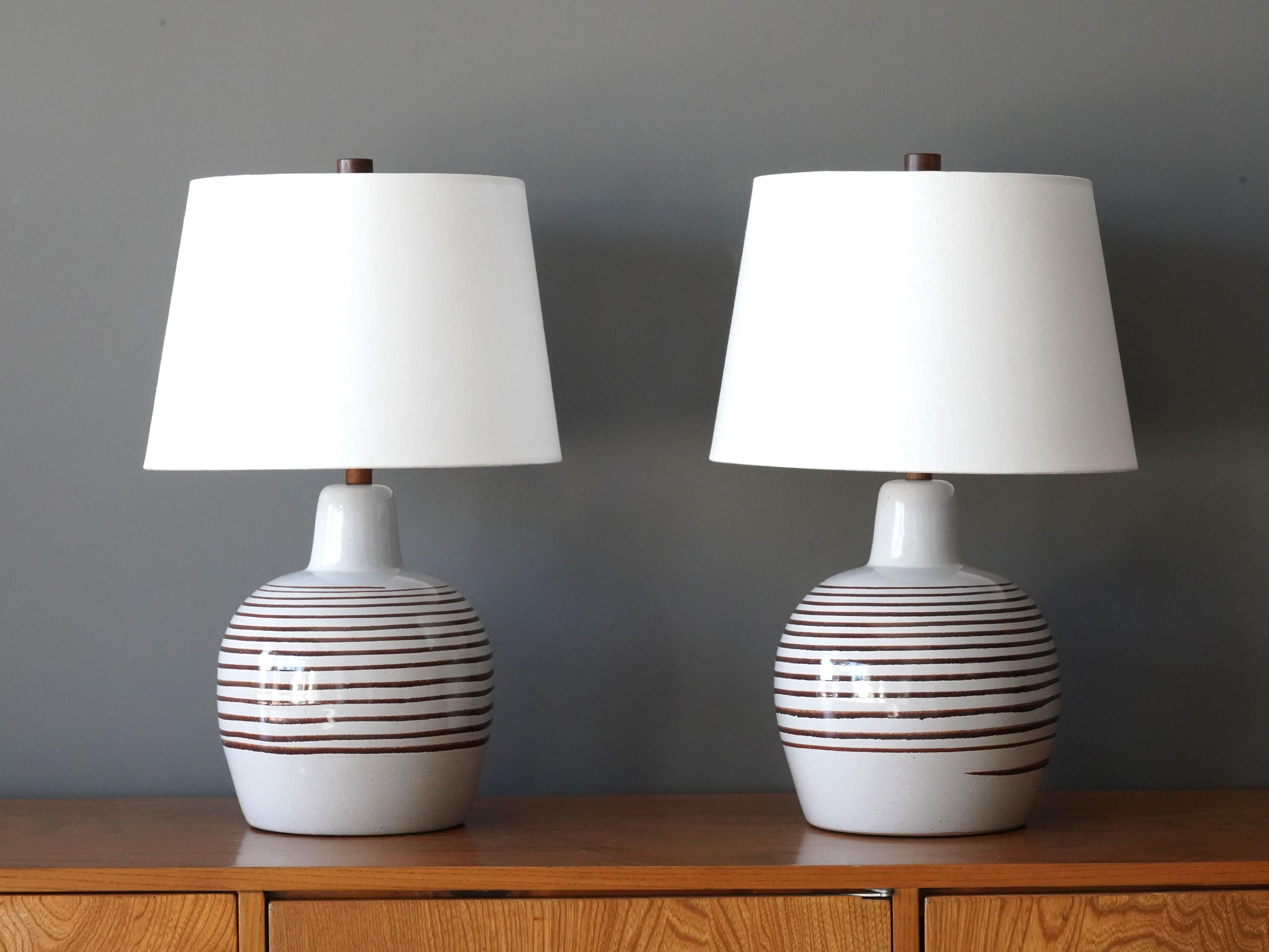 A pair of table lamps designed by husband and wife duo Jane & Gordon Martz. Produced by Marshall Studios, Indianapolis. 

Bases are slip-cast and then dipped into glaze and hand painted. Design also incorporates exquisite walnut necks and finials.