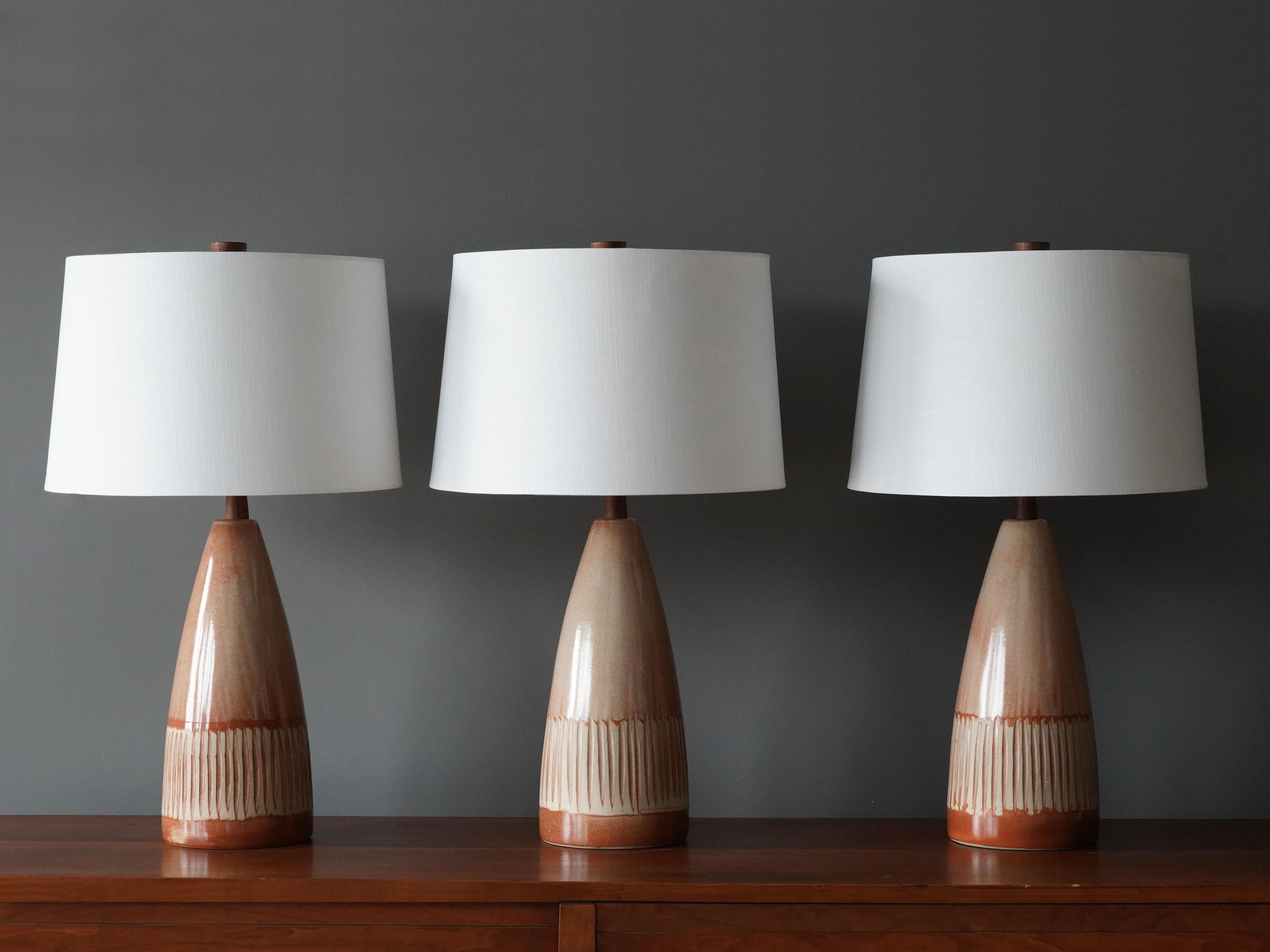 A pair of table lamps designed by husband and wife duo Jane & Gordon Martz. Produced by Marshall Studios, Indianapolis. 

The bases are slip-cast and then dipped into glaze and hand painted. Design also incorporates exquisite walnut necks and