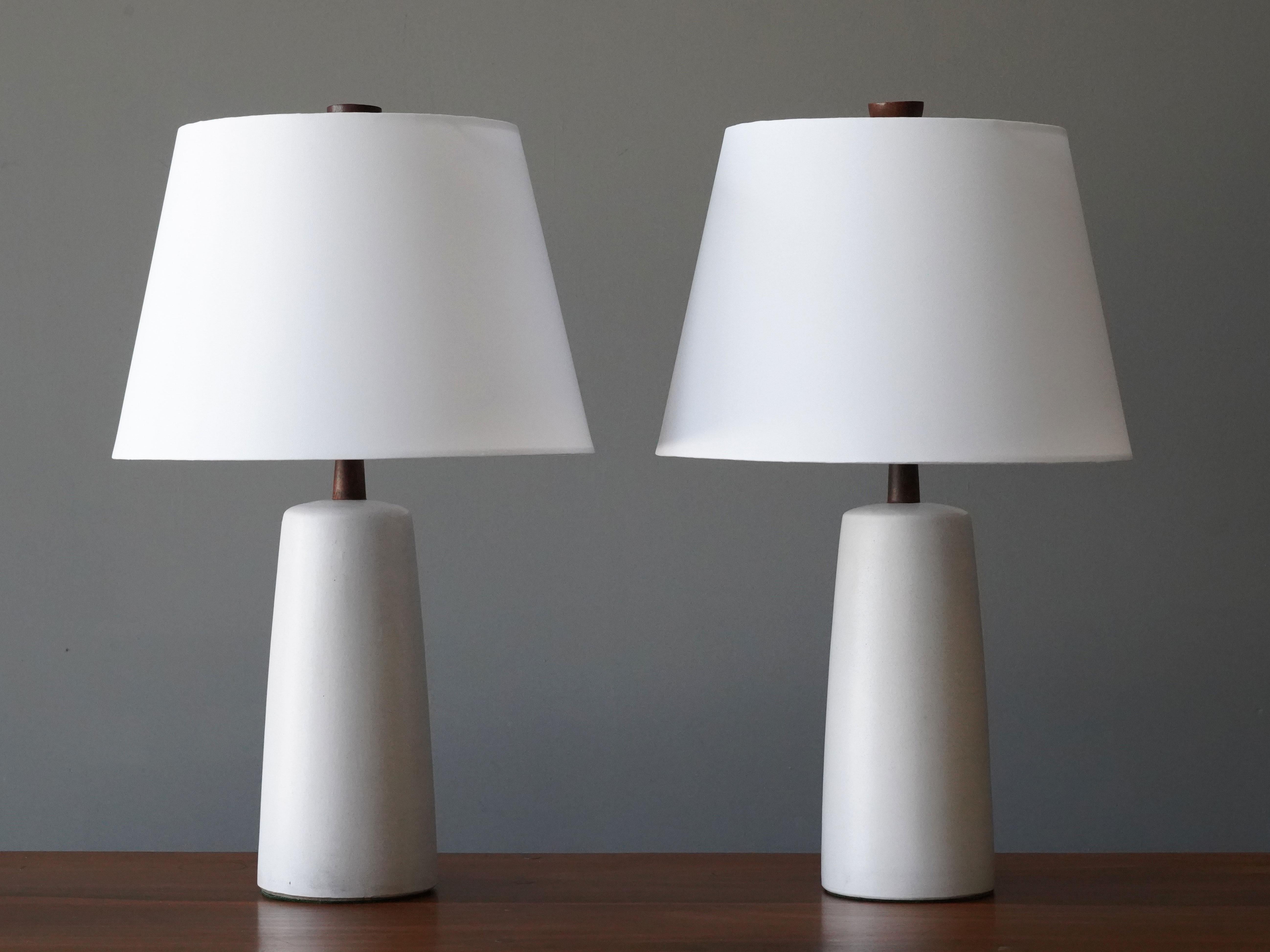 A pair of table lamps designed by husband and wife duo Jane & Gordon Martz. Produced by Marshall Studios, Indianapolis. 

The off white bases are slip-cast and then dipped into glaze. Design also incorporates exquisite walnut necks and finials.