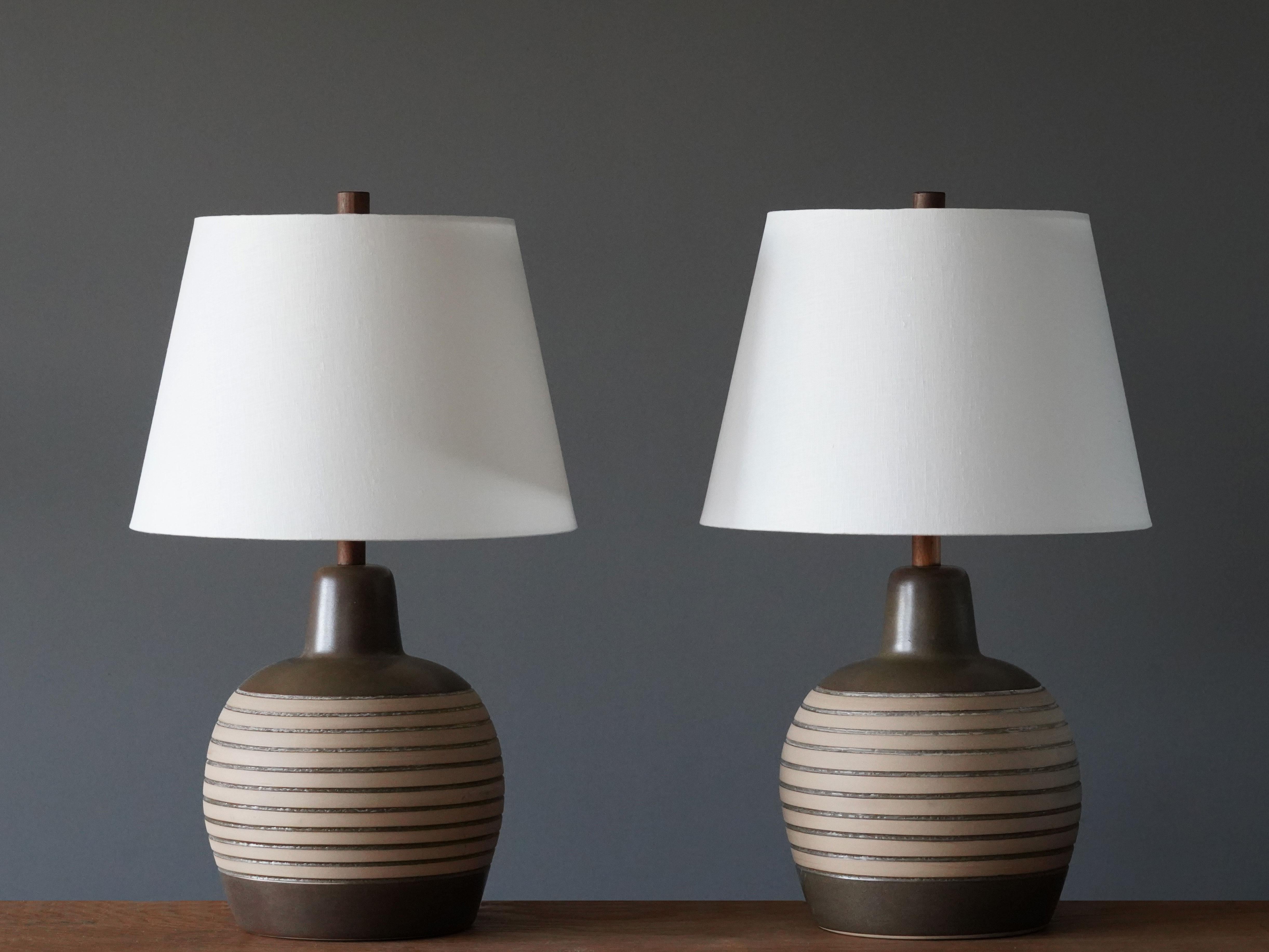 A pair of table lamps designed by husband and wife duo Jane & Gordon Martz. Produced by Marshall Studios, Indianapolis. 

The base is slip-cast and then dipped into glaze and hand painted. Design also incorporates exquisite walnut neck and finial.