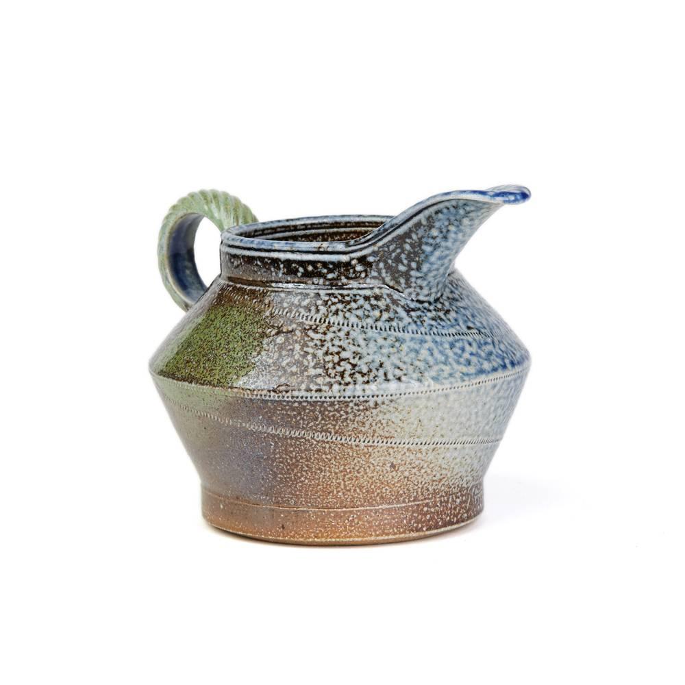 A stylish vintage British studio pottery pot and cover by renowned potter Jane Hamlyn and made at Millfield Pottery near Doncaster. The rounded shaped jug has a rope twist rounded handle with a large raised pouring spout the body with wheel cut