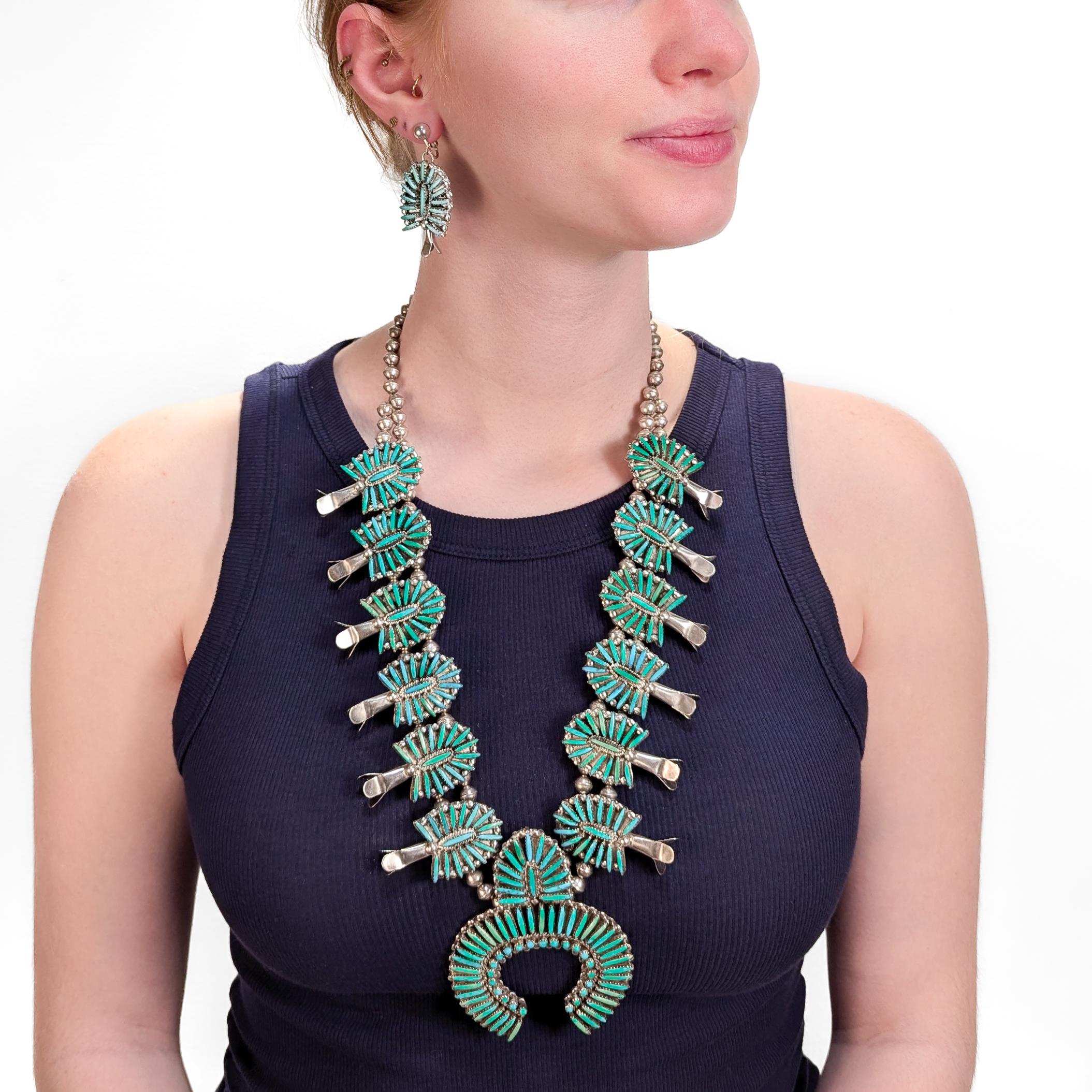 Una raffinata collana di fiori di zucca e orecchini demi-parure vintage di Zuni.

Di Jane L. Peynetsa.

In argento sterling. 

Collana a forma di fiore di zucca con cabochon di turchese a punto croce e orecchini a clip abbinati.

Marcato sul retro.
