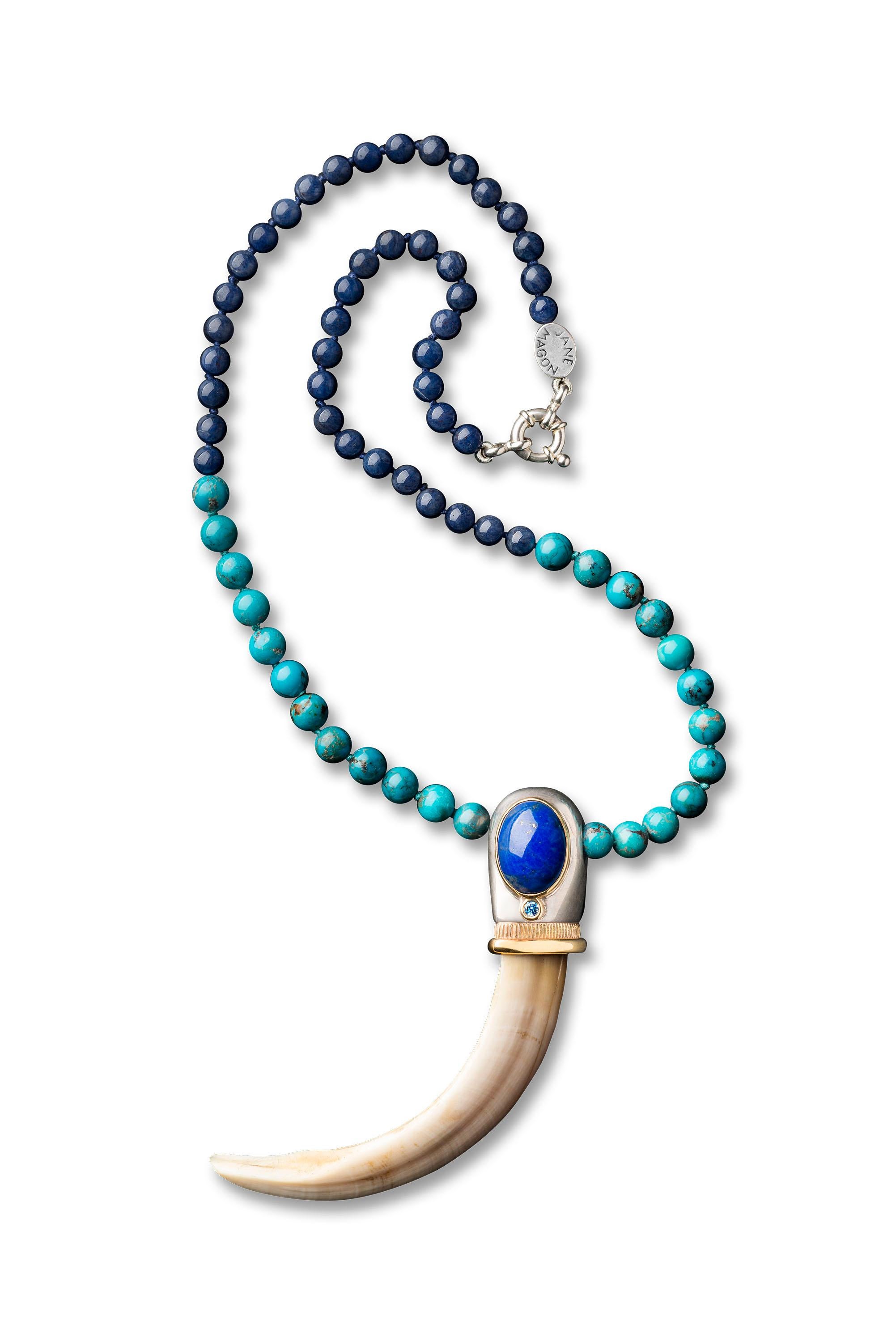 Jane Magon Collections Warrior Woman Tush Necklace has a Razorback Boar Tusk with a 9kt Yellow Gold Bezel setting holding it and a Round Blue Topaz and a large Cabochon Lapiz Lazuli Stone. Set on a Lapiz Lazuli bead and Turquoise Bead Necklace. Has