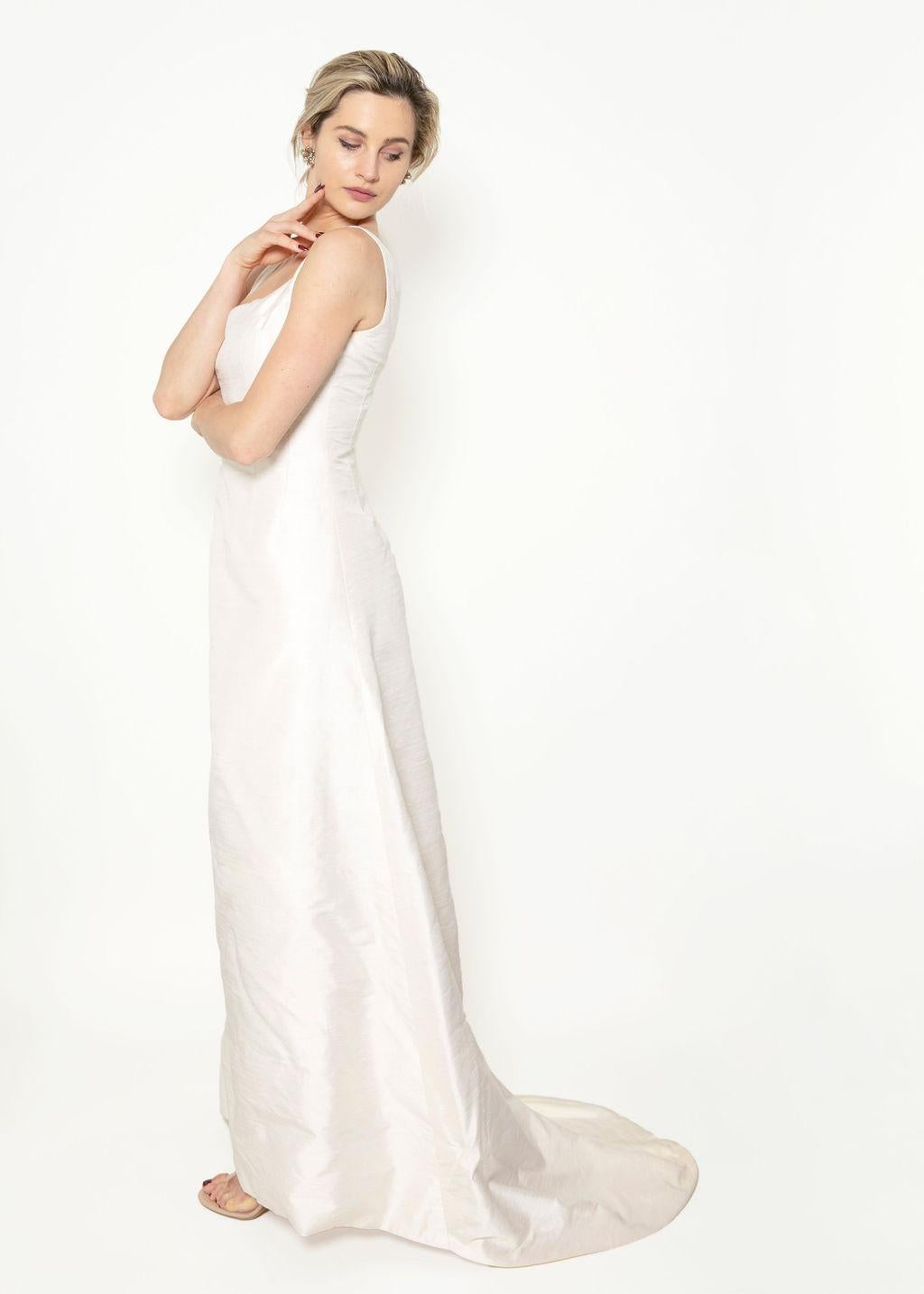 Schreiten Sie mit dem weißen Kleid mit Schleppe von Jane Marquis im Stil der 1960er Jahre mit raffinierter Eleganz zum Traualtar. Dieses Brautkleid mit klassischer Linienführung und 1-Zoll-Trägern hat eine anmutige Schleppe und einen Reißverschluss