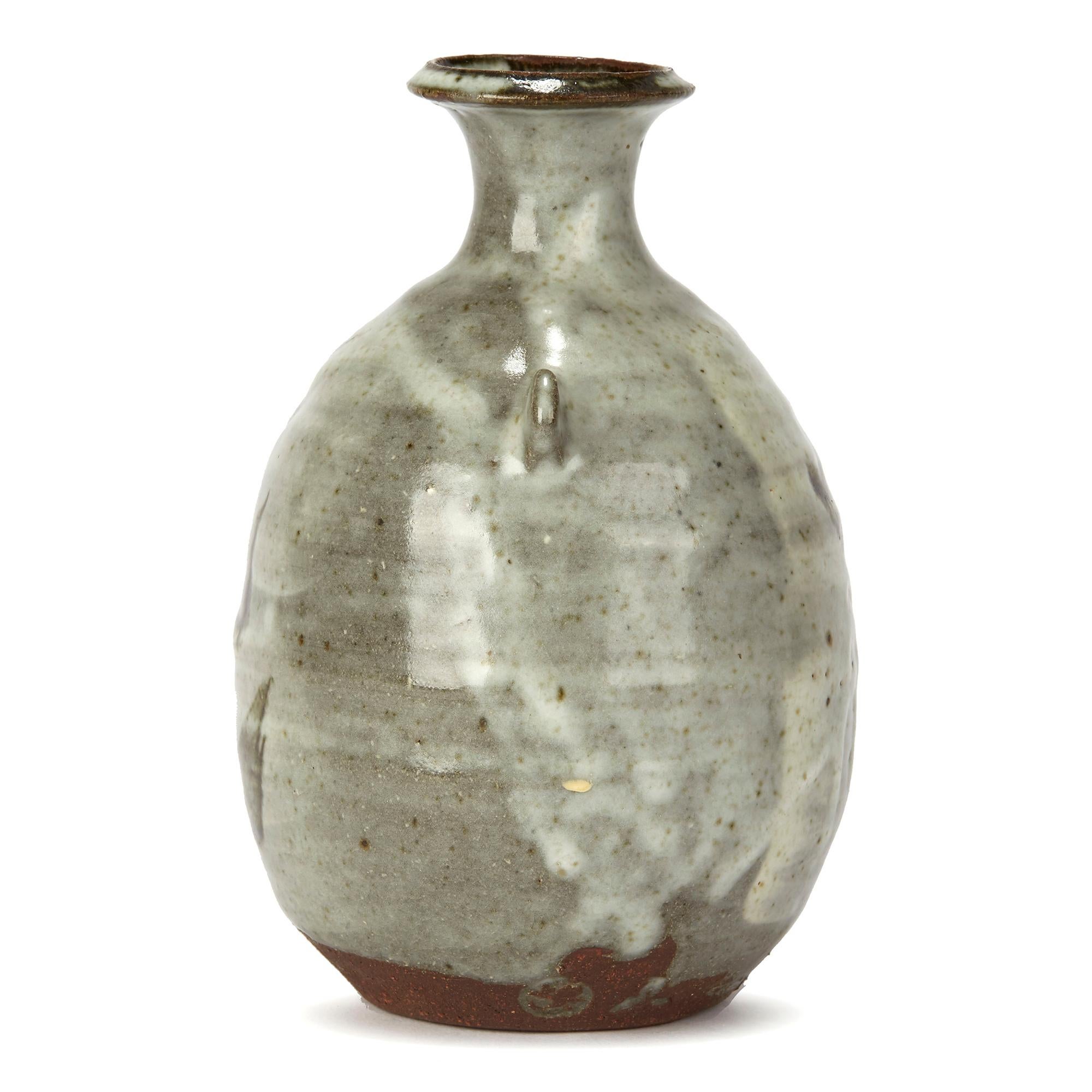 A stylish Leach pottery stoneware bottle shaped studio pottery vase decorated with contrasting abstract bird like designs set within expressive white run splashes on a stone grey ground by renowned potter Janet Leach (American, 1918-1997). The