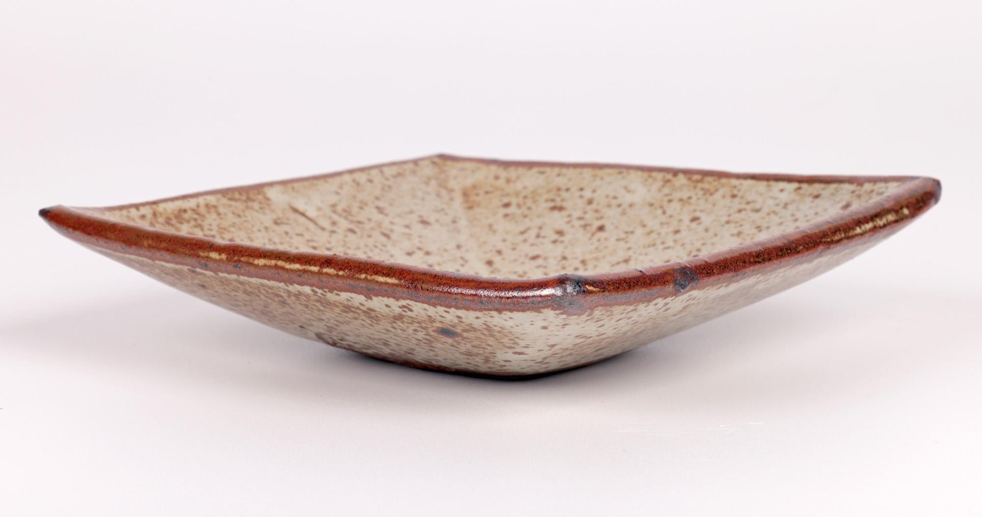 A stylish stoneware studio pottery square form Repeat ware dish by renowned studio potter Janet Leach (British, 1918-1997) dating from around 1960. The dish stands on a narrow unglazed foot with a slight recessed base with raised square formed