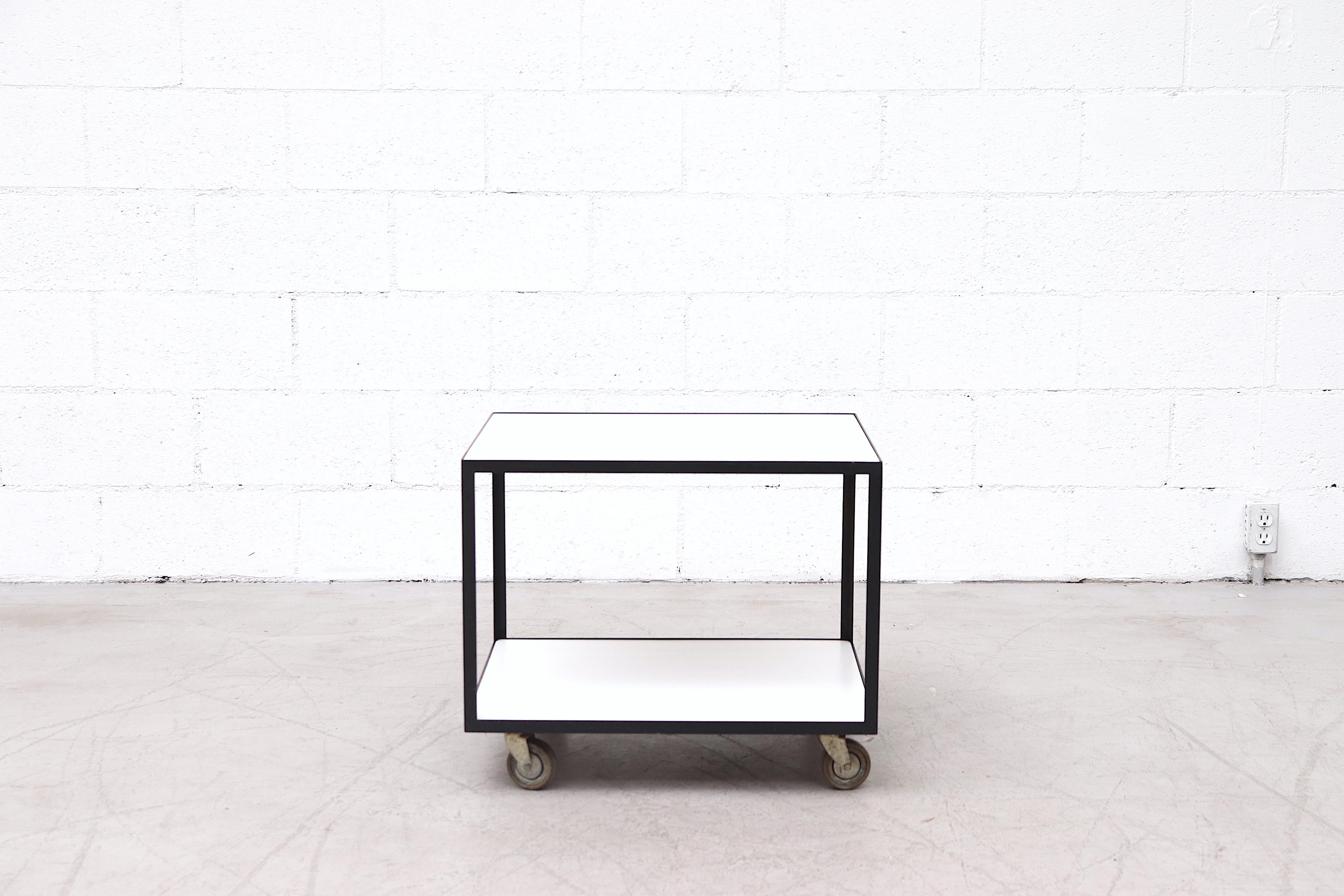 Janni Van Pelt style rolling bar cart with black enameled metal frame and inset white formica surfaces. In original condition with visible wear and some enamel loss.