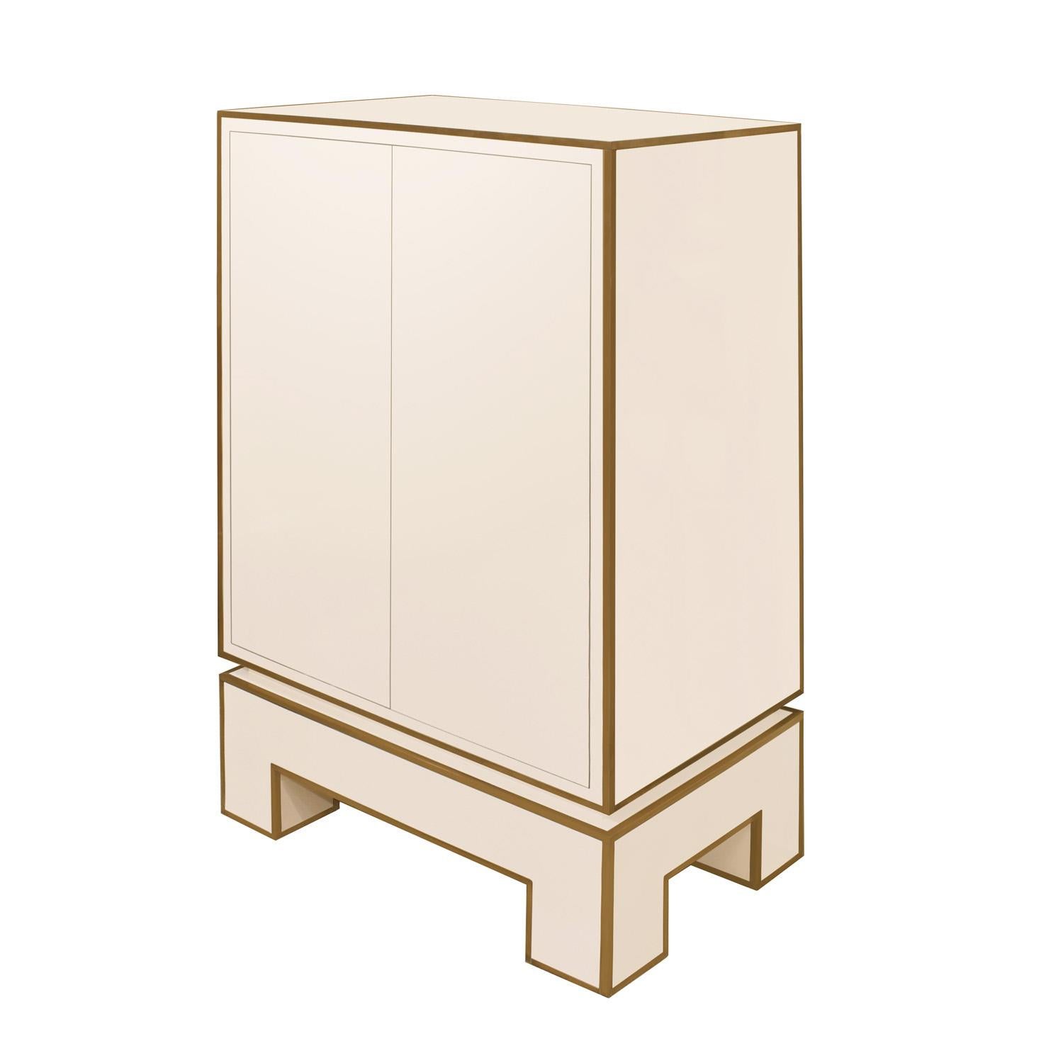 Chic 2 door cabinet in ivory lacquer with brass trim by Alain Delon for Maison Jansen, France 1975 (brass label with designer signature inside left door). This cabinet was part of a series by the designer shown at the 1975 Salone del Mobile in