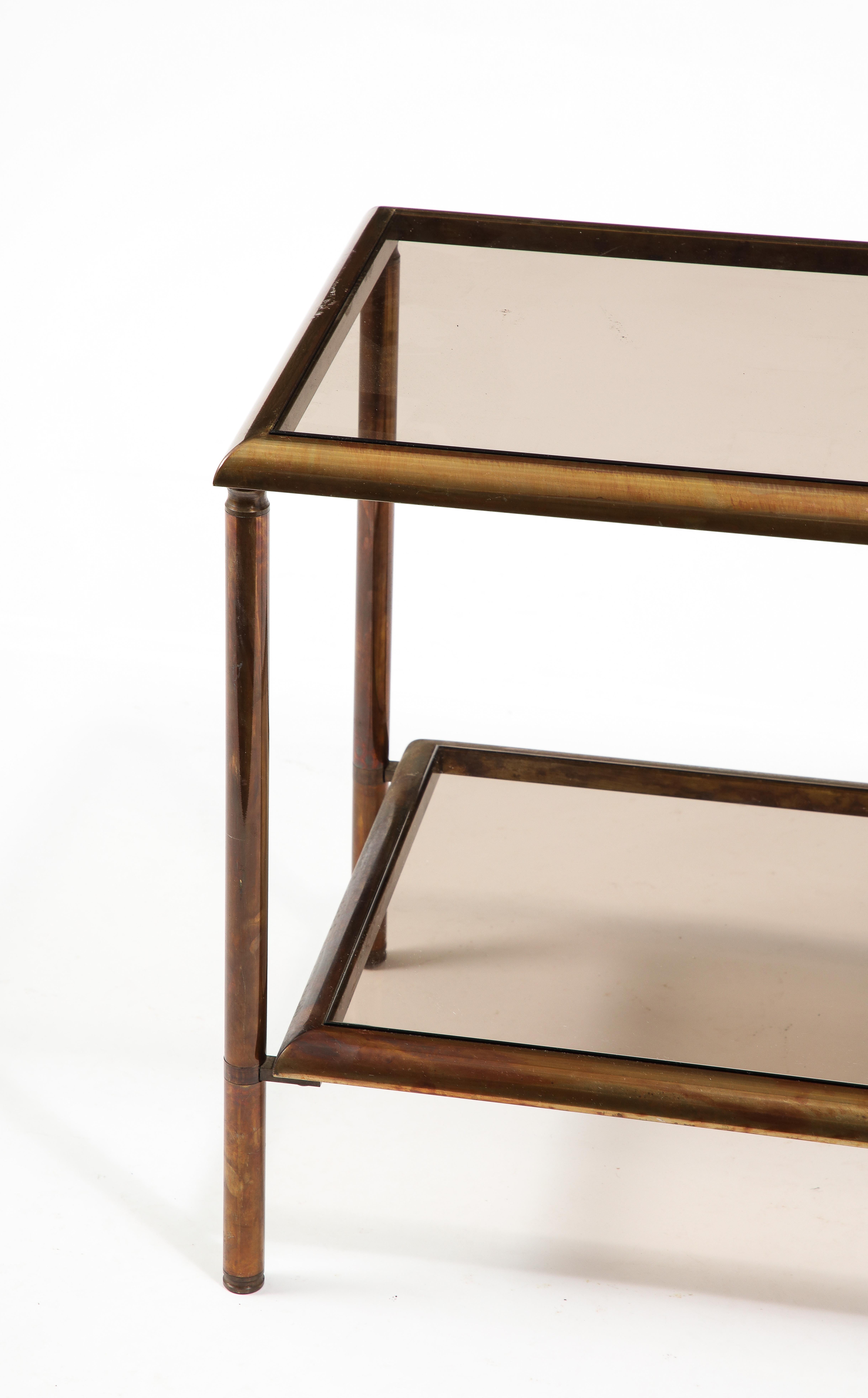 Patinated Bronze and smoked glass end tables, the tiers have curved solid trims connected to round uprights. 
