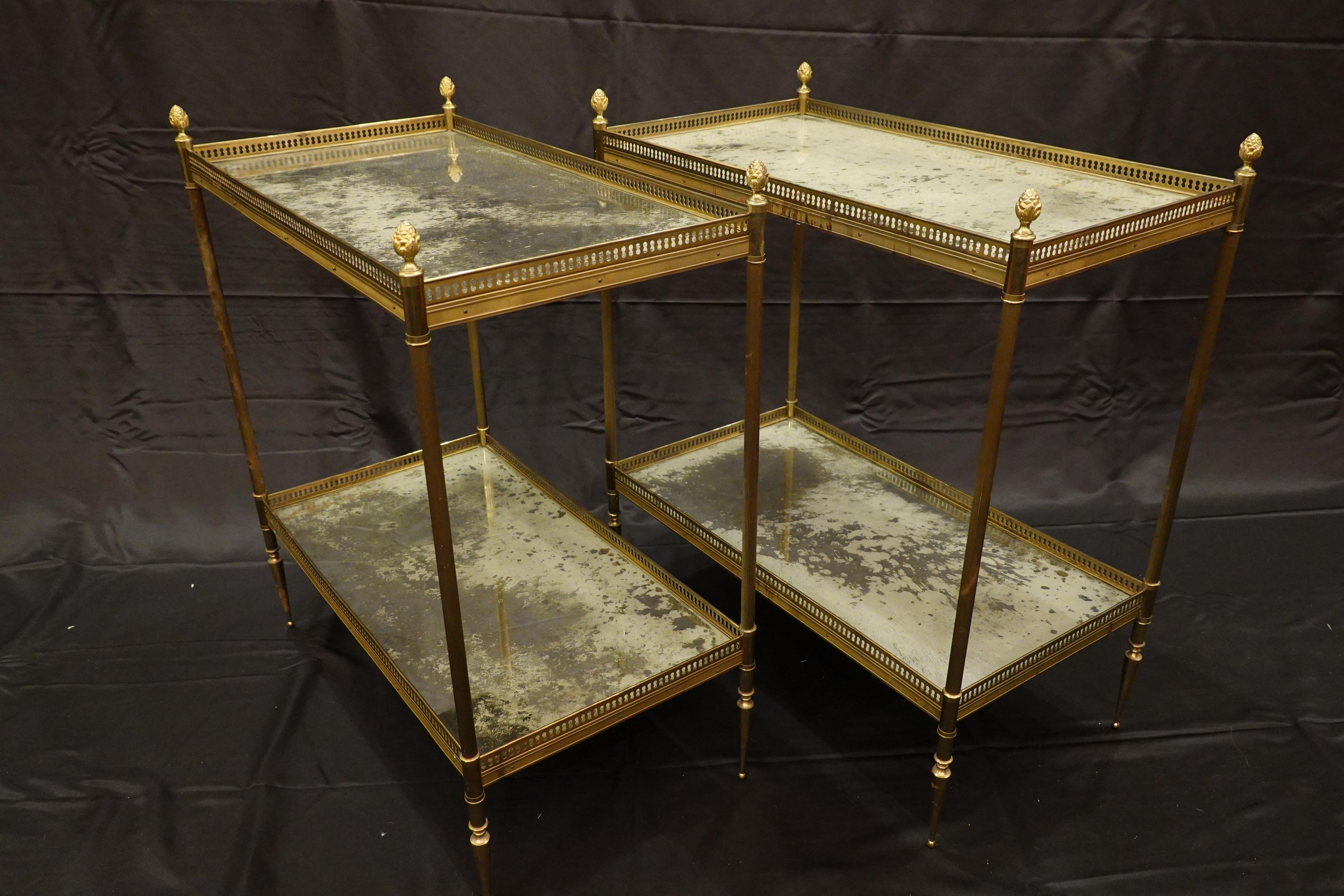 Pair of French brass two-tiered side tables, with églomisé tops and detailed brass and bronze frames, attributed to Maison Jansen. The tables feature pierced galleries, fluted legs topped with gilded bronze pine cone finials and ending in tapered