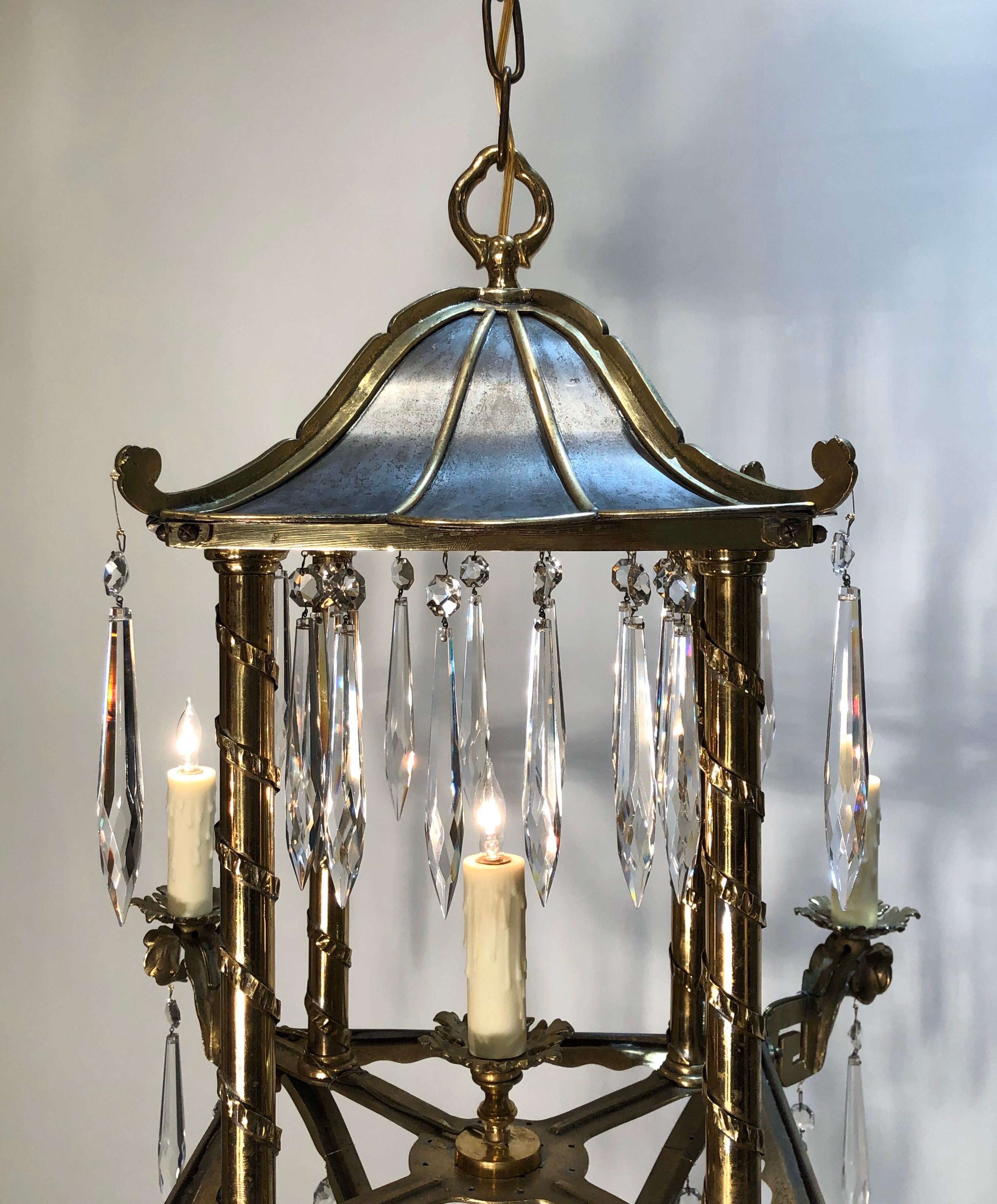This elegant Jansen style lantern has a two-tone silver and brass finish. The Lantern has a detailed pagoda top with crystal prisms. The top is held up by four columns wrapped in vines sitting on a brass framed console with candle lights on the