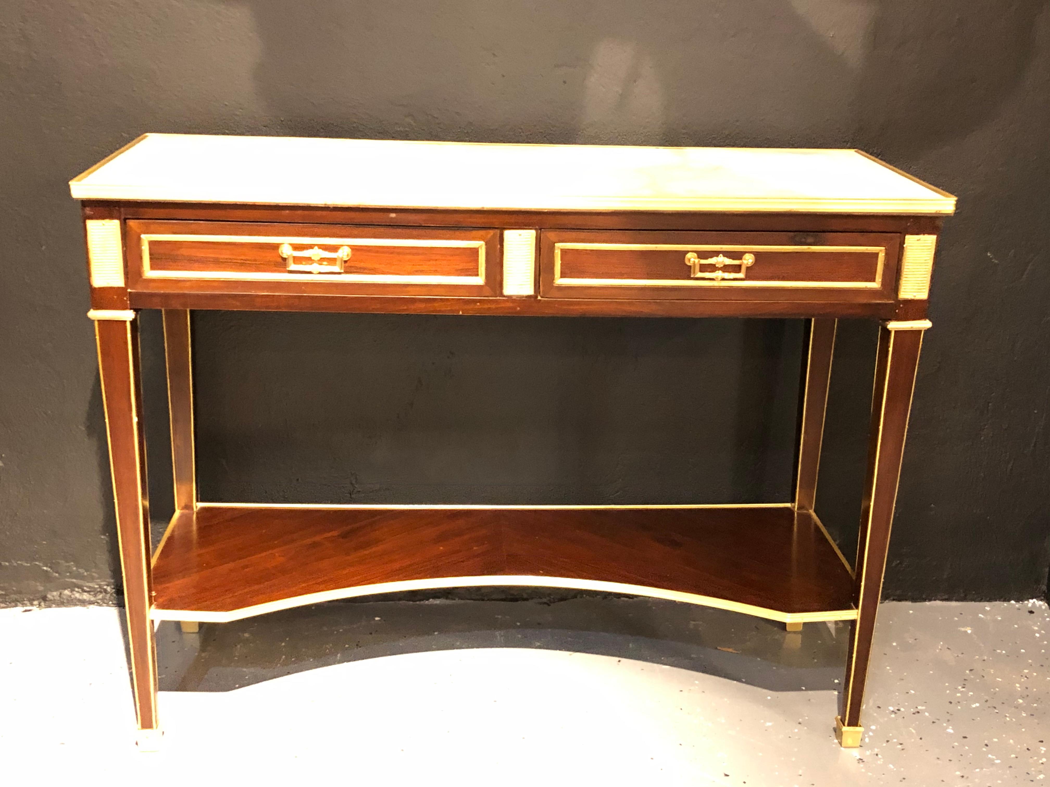 Jansen style two-drawer marble-top bronze console or serving table. Having a bronze framed white marble top supported by an oak secondary case of two drawers with bronze framing, flanked by bronze cookie cutter corners and center having an inverted