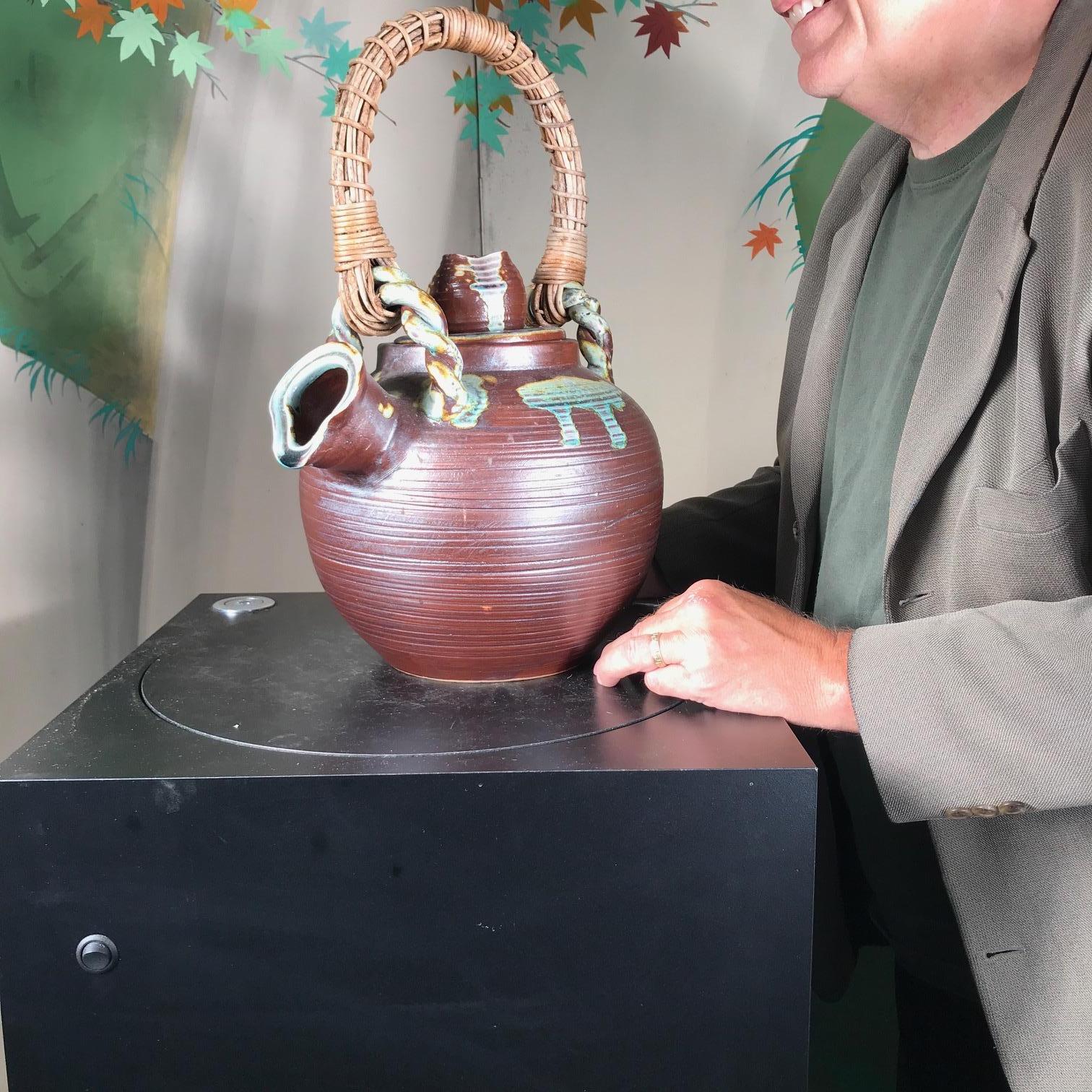 A superb Japanese oversized tea pot form flower or water vessel handcrafted in beautiful Classic Shigaraki glazes: blue greens over cream and reddish clay in an organic floral pattern. The fine rattan handle completes this two piece beautiful work