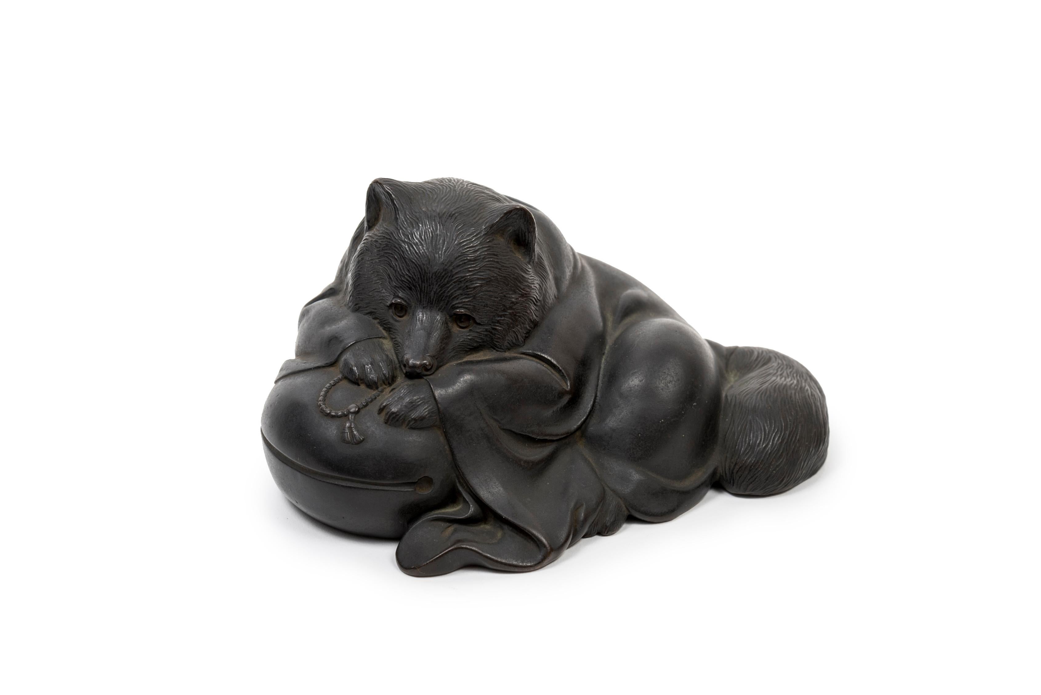 Japanese bronze sculpture of a tanuki. It represented as a Buddhist priest, wrapped in a cloak and lying on a mokugyo (a percussion instrument made of a fish-shaped wooden block and a stick, used to accompany the recitation of sutras).

The tanuki