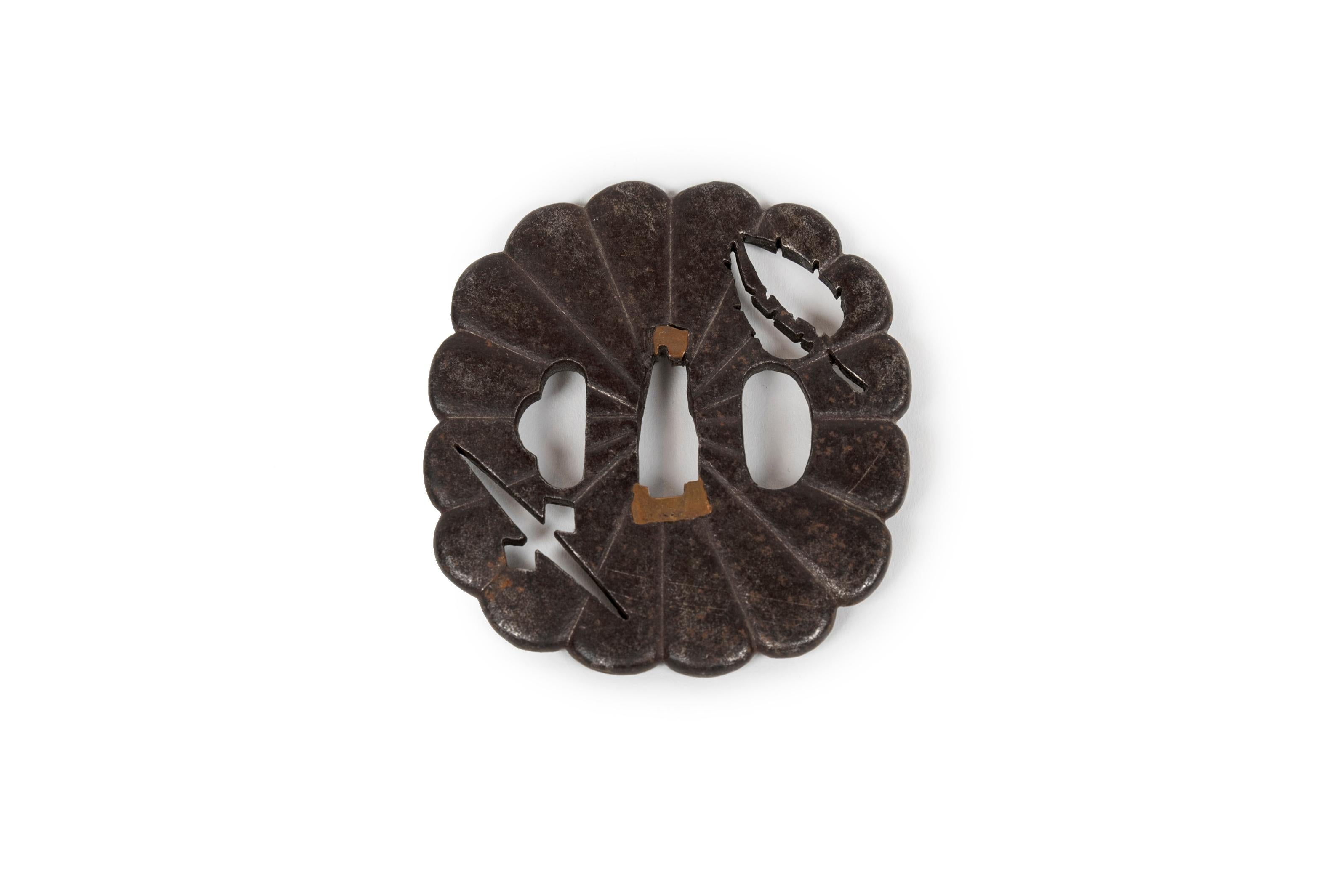 Eiserne Tsuba in Form einer Chrysantheme (Kikugata), durchbrochen im Negativ mit Blattwerk und geometrischen Mustern.

Chrysanthemenförmige Tsuba waren in der Edo-Zeit sehr beliebt, da die Blume als Symbol für Adel und Eleganz galt. Kikugata sind