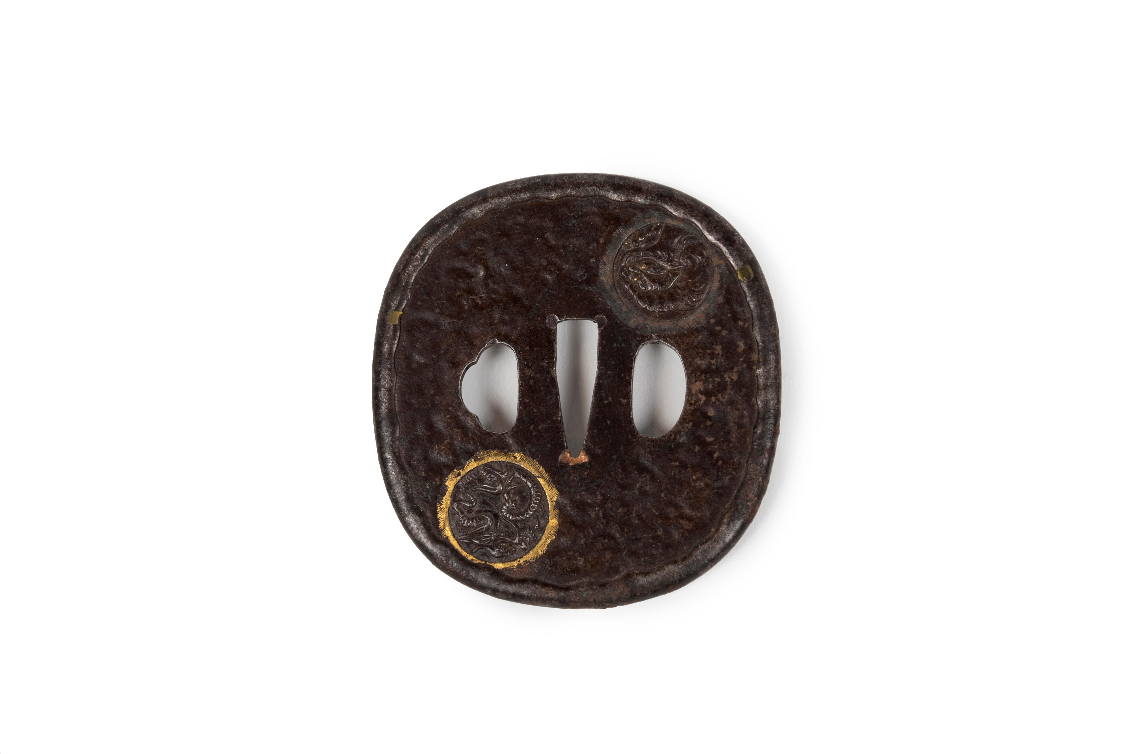 Eiförmige (nagamarugata) Eisen-Tsuba, gehämmert und mit Medaillons getrieben. Auf der einen Seite befinden sich Medaillons mit einem Drachen mit goldenen Akzenten und einem Komainu (oder Shishi - Löwenhund, der den Tempel bewacht). Auf der anderen