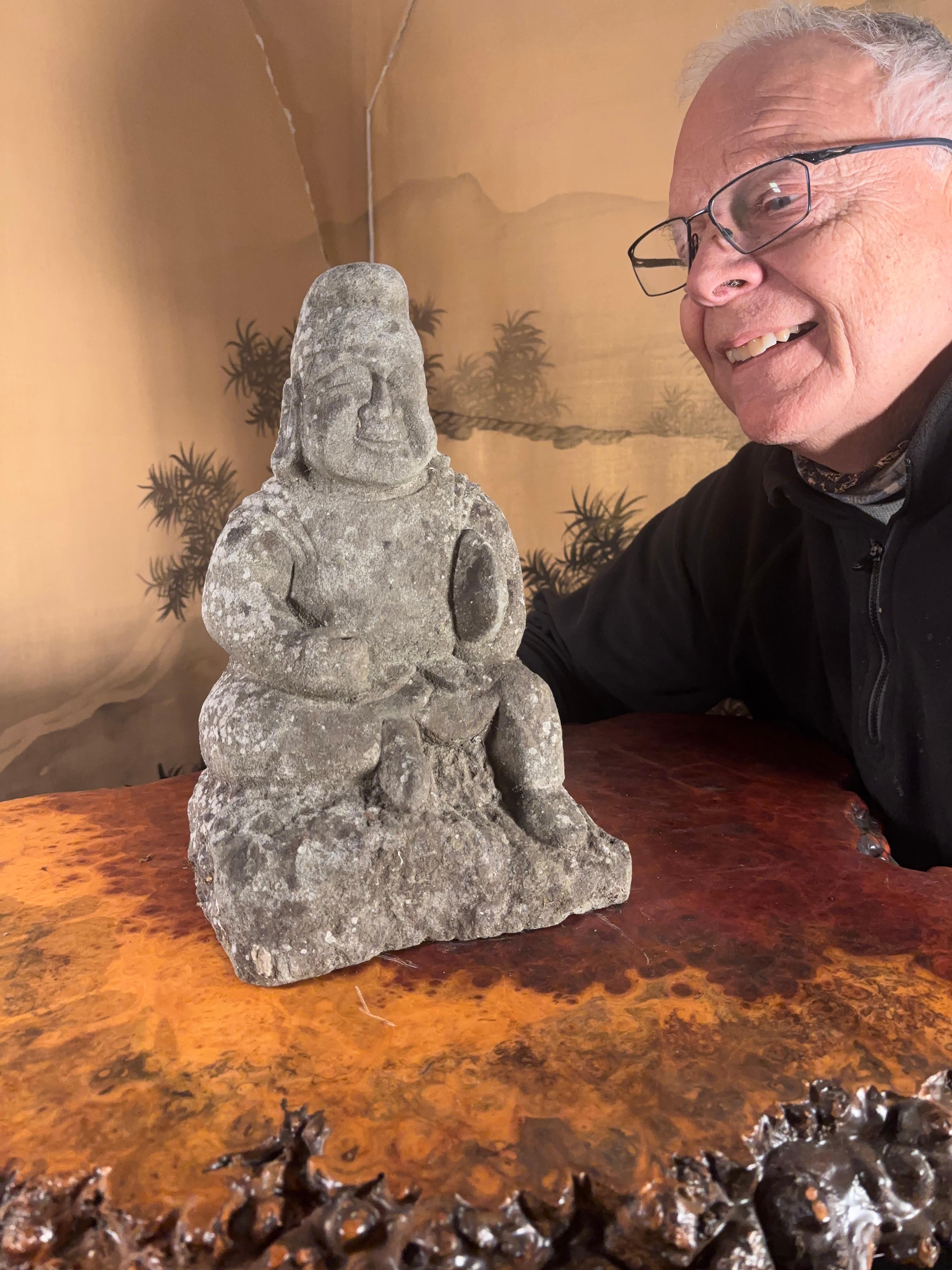 Japan, an old early 20th century tall hand-carved stone image of Ebisu one of Japan's seven lucky gods signifying prosperity, good business, and patron of fishermen, circa 1920.  He sits upon an outcrop wearing his notable pointed hat and clutching