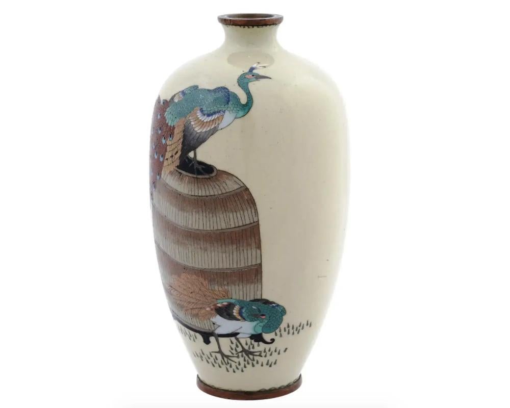 An antique Japanese Meiji period enamel over brass vase. The vase has an amphora shaped body and a narrow neck. The vase is enameled with a polychrome scene with a pair of peacocks made in the Cloisonne technique on beige ground. Unmarked. Circa: