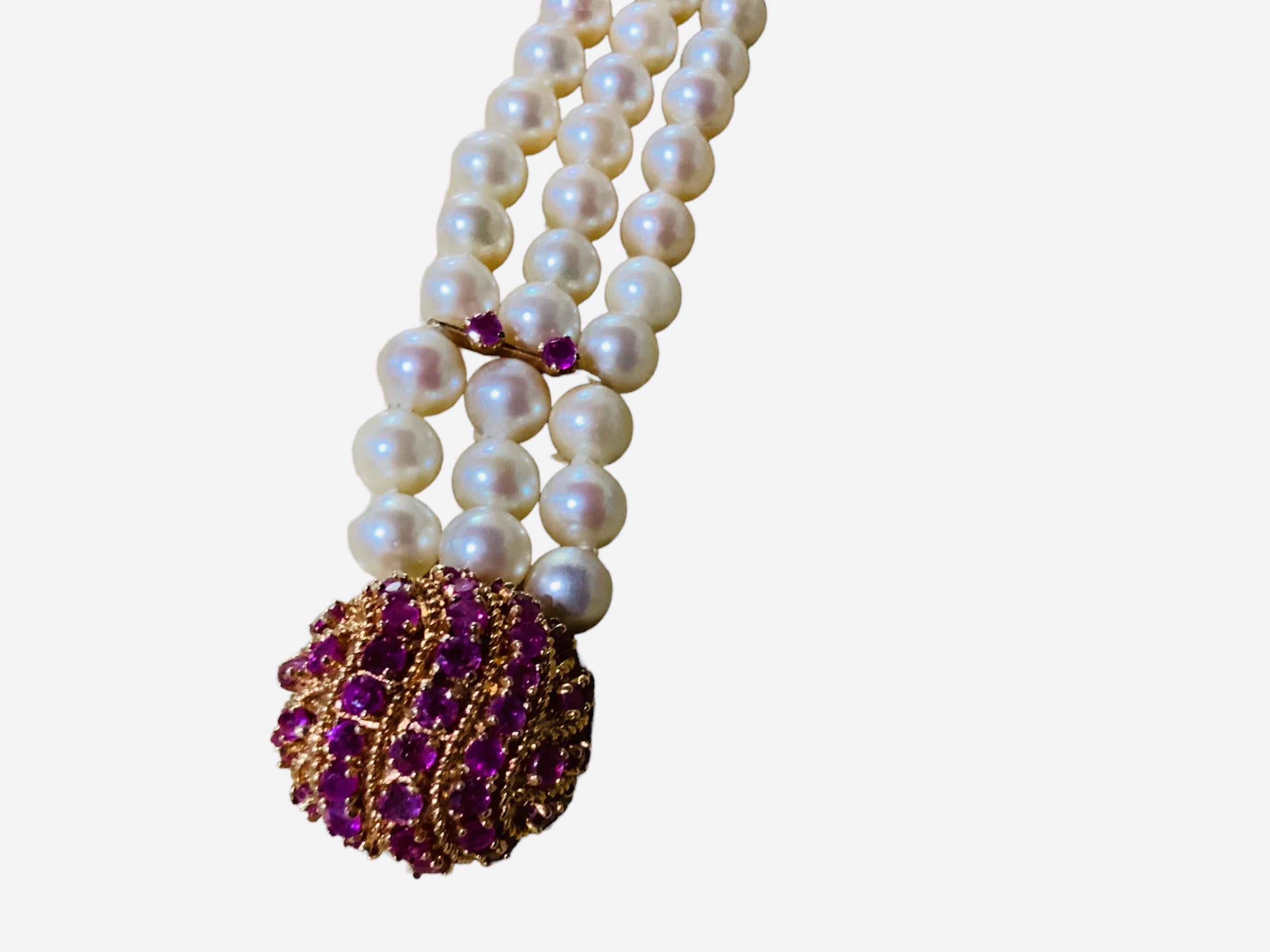 This is a Japanese 14K gold culture pearls and rubies bracelet. It depicts three strands of pearls, for a total of 60 pearls. Each pearl measuring between 7.0-7.4mm each one. Two rubies ( 3.1mm in diameter) in 14K gold prongs setting adorn after
