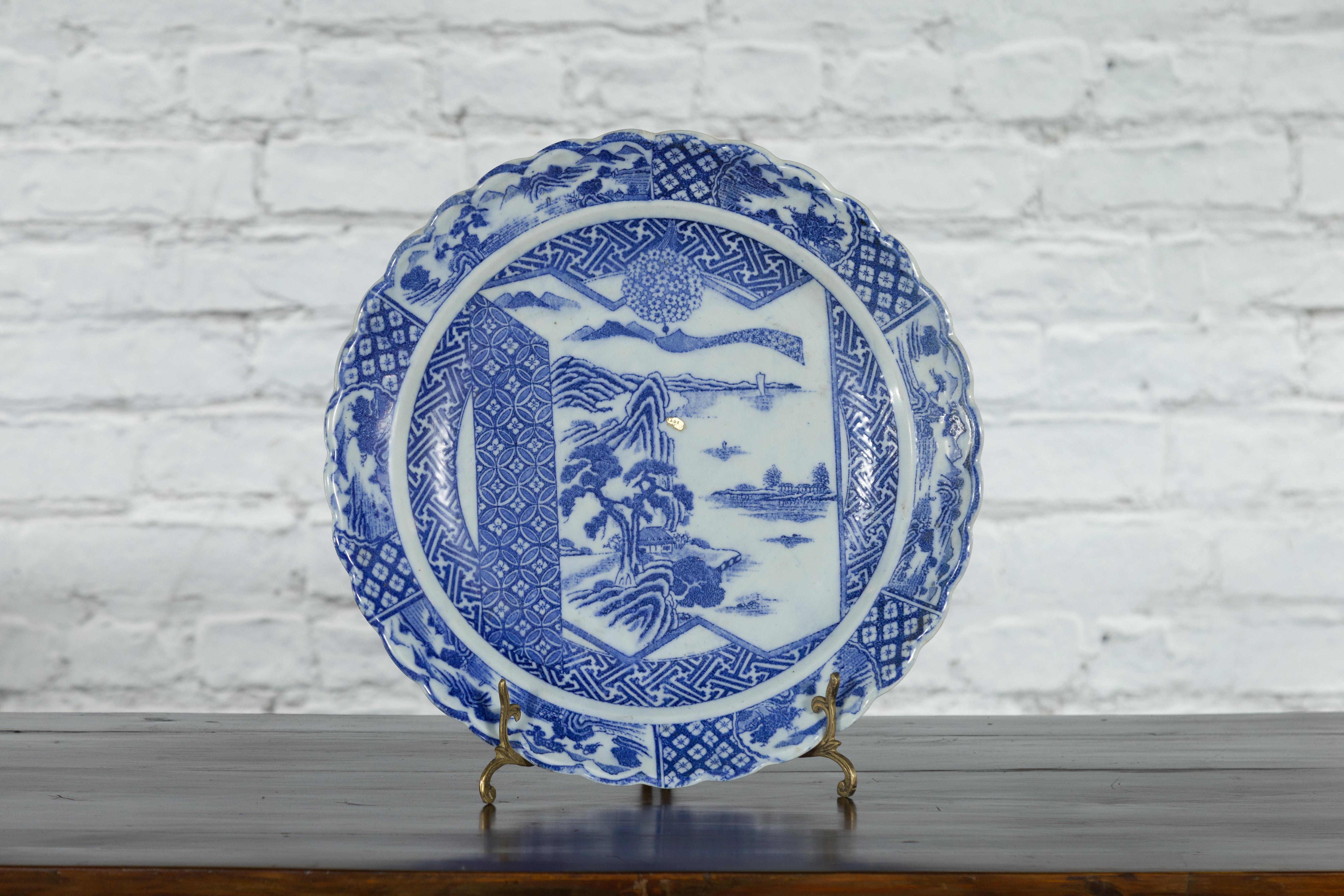 A Japanese porcelain plate from the 19th century, with hand-painted blue and white mountainous landscape and architecture décor, surrounded by geometric motifs. Created in Japan during the 19th century, this porcelain plate features a delicate blue