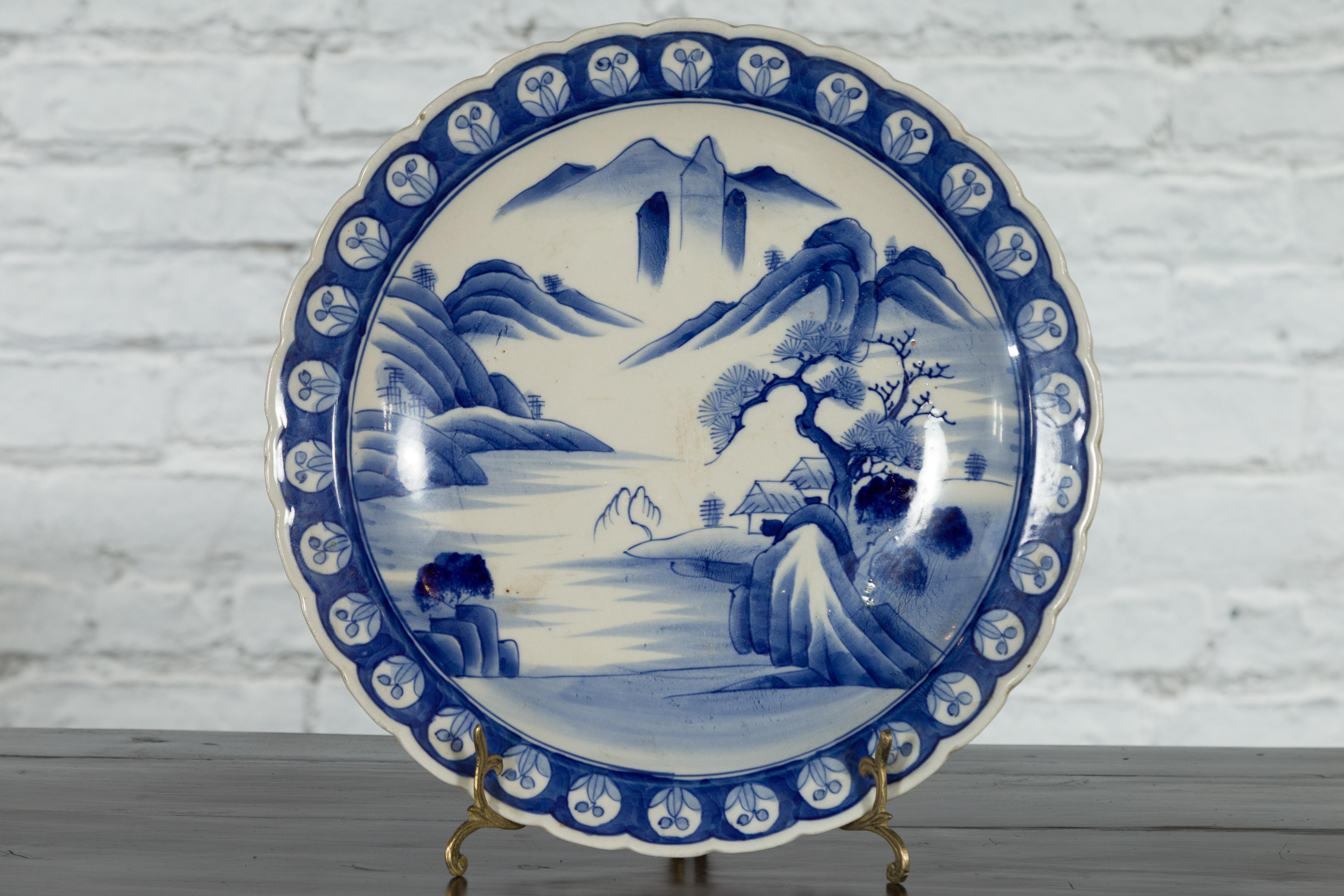 A Japanese porcelain plate from the 19th century, with hand-painted blue and white mountainous landscape and architecture décor. Created in Japan during the 19th century, this porcelain plate features a delicate blue and white décor depicting an