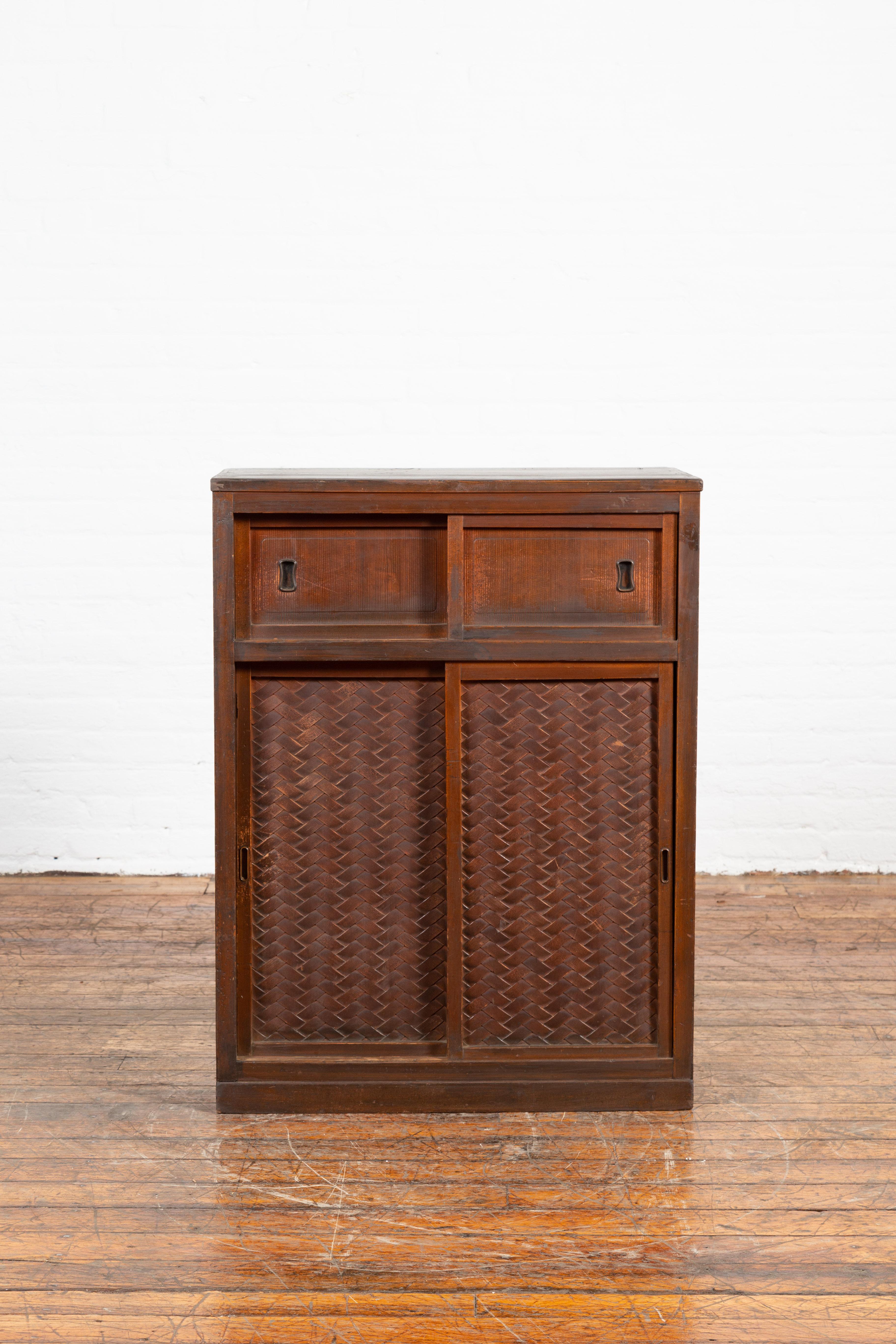 A Japanese antique cabinet from the 19th century, with woven criss-cross design, sliding doors and hidden drawers. Created in Japan during the 19th century, this cabinet features a rectangular top sitting above two narrow sliding panels. It is the