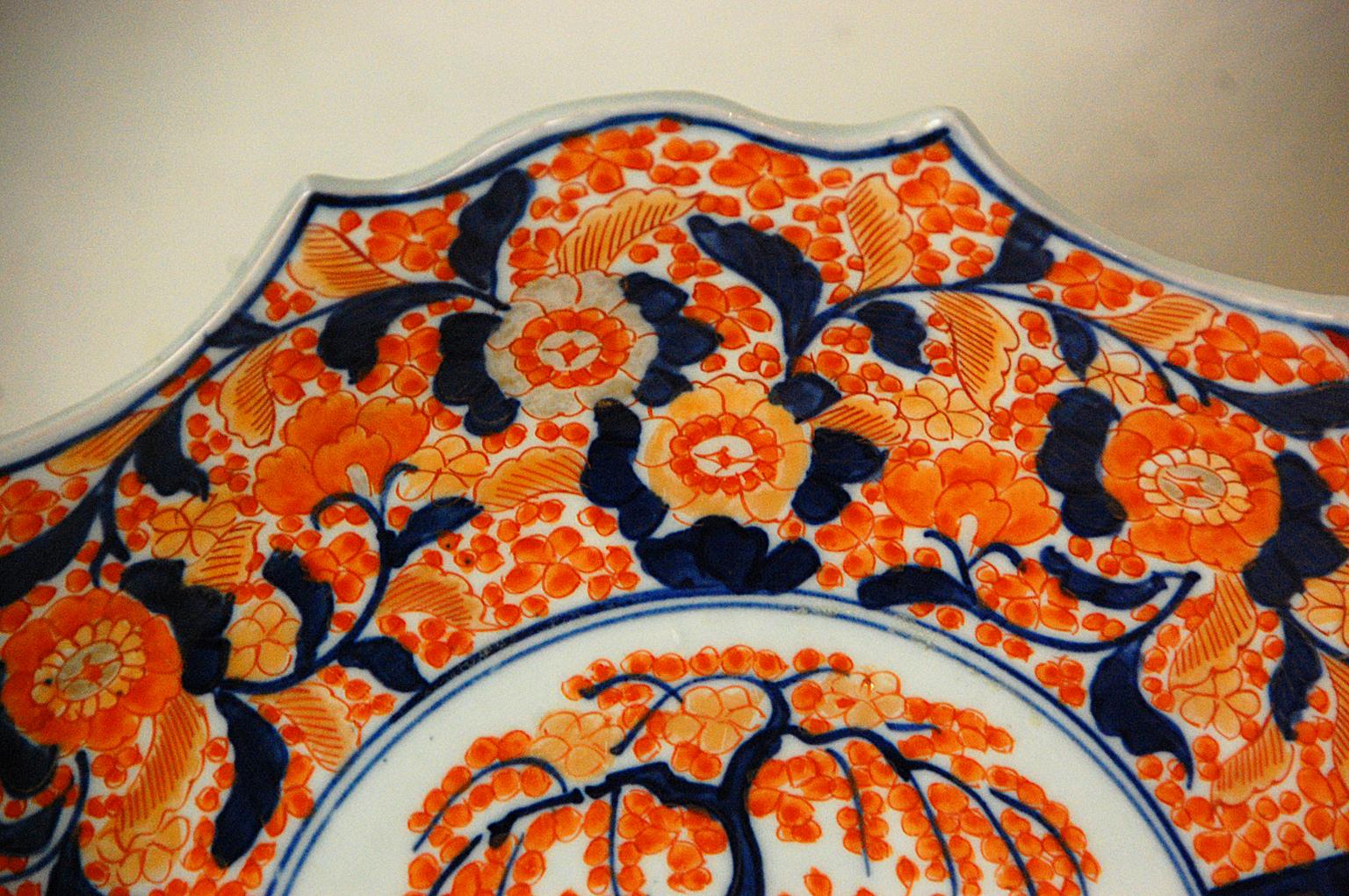 Japanese 19th century Meiji period Imari 12 inch charger. This unusually shaped charger is hand painted with underglaze blue and overglaze enamels highlighted by gold leaf detailing. The central panel is populated by a jardinière filled with a