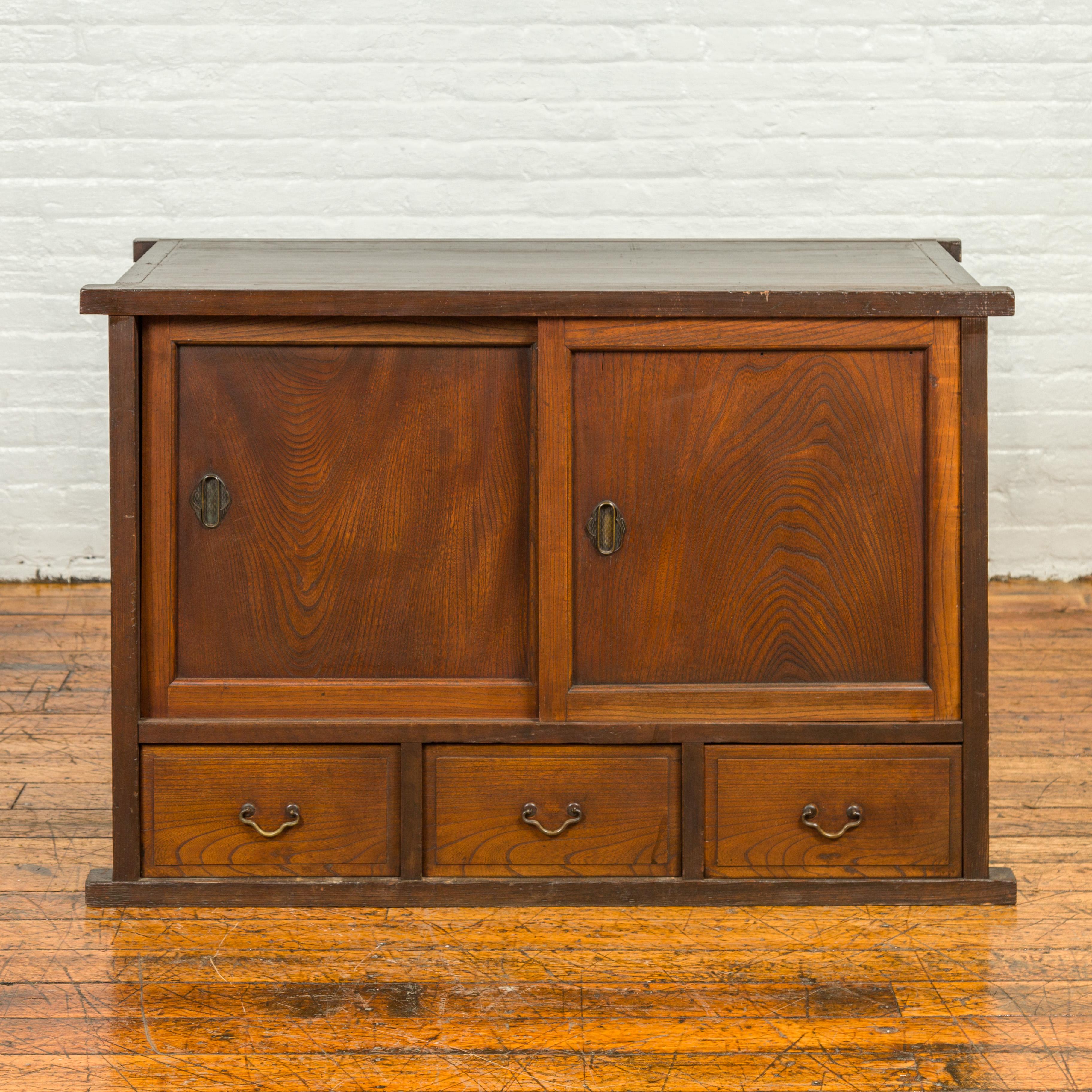An antique Japanese keyaki wood buffet from the 19th century, with sliding doors and three drawers. Crafted in Japan during the 19th century, this keyaki wood buffet features a rectangular top with protruding corners, sitting above two sliding doors