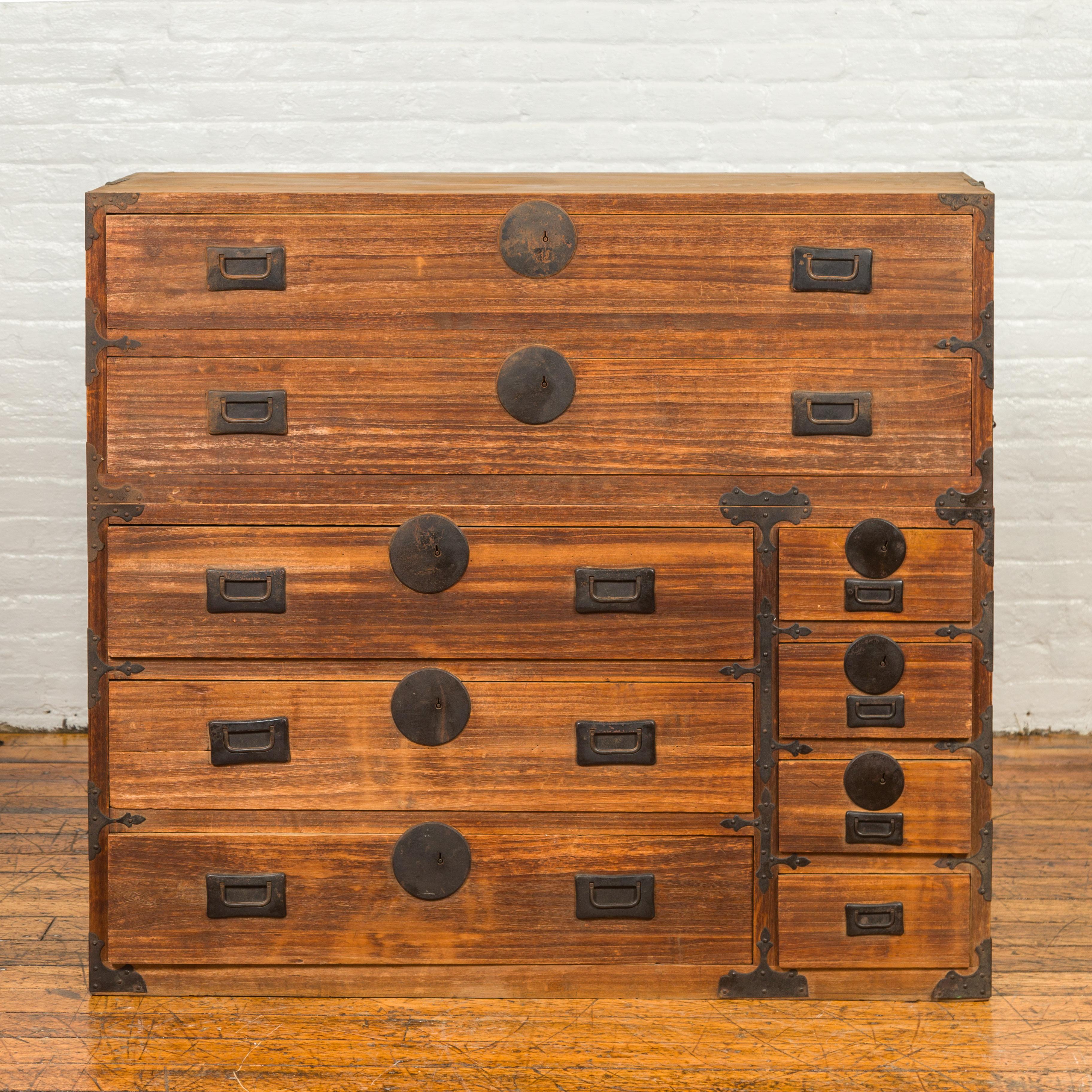 A Japanese Meiji period kiri wood two-section tansu clothing chest from the 19th century with multiple drawers, iron hardware and medallions. Crafted in Japan during the Meiji period, this kiri wood tansu chest captures our attention with its