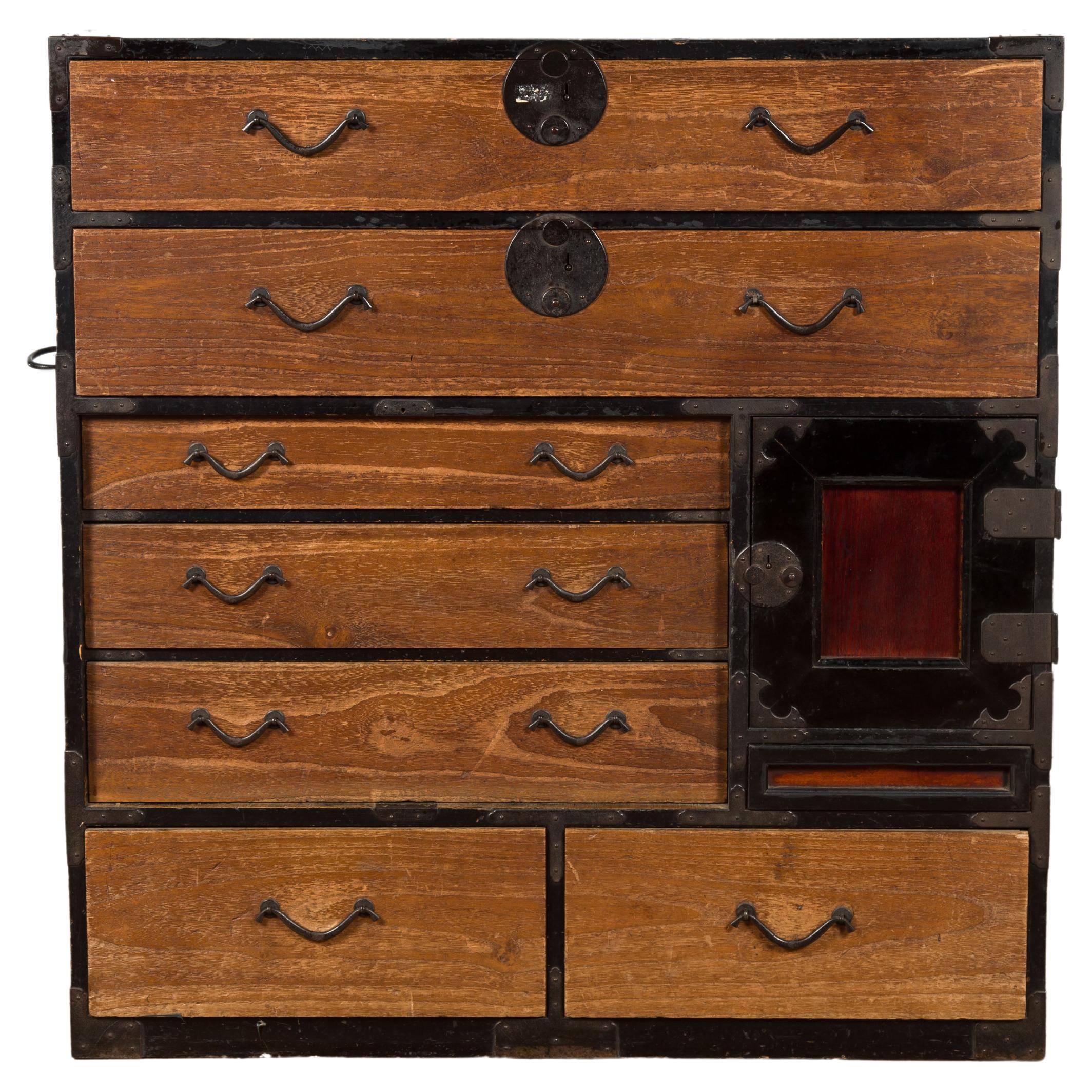 An antique Japanese Meiji period tansu clothing chest from the 19th century, with black and brown patina. Created in Japan during the 19th century, this tansu chest features a rectangular top sitting above seven drawers surrounding a side door