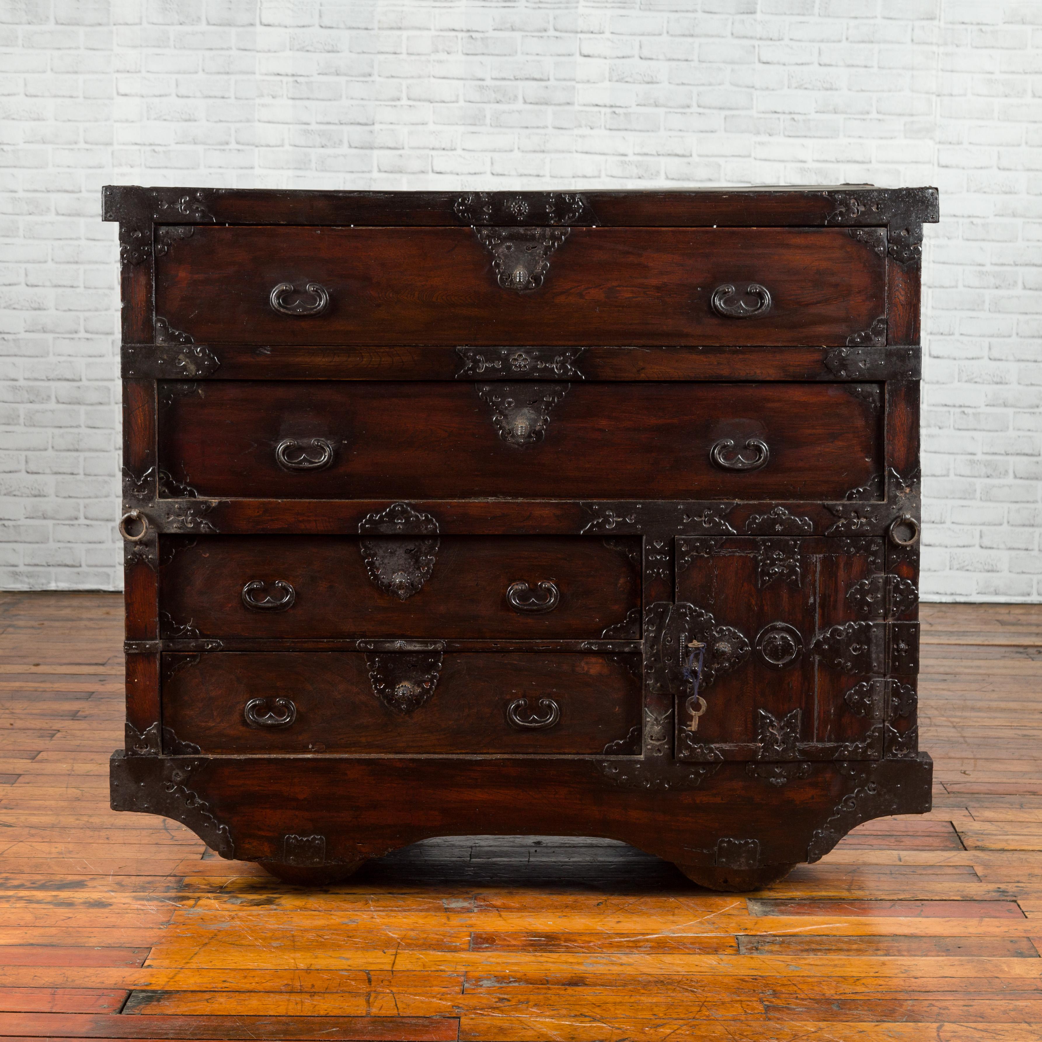 A Japanese merchant's chest from the 19th century, with four large drawers and a lateral door concealing additional drawers. Created in Japan during the 19th century, this merchant's chest features a dark brown patina perfectly complimented by