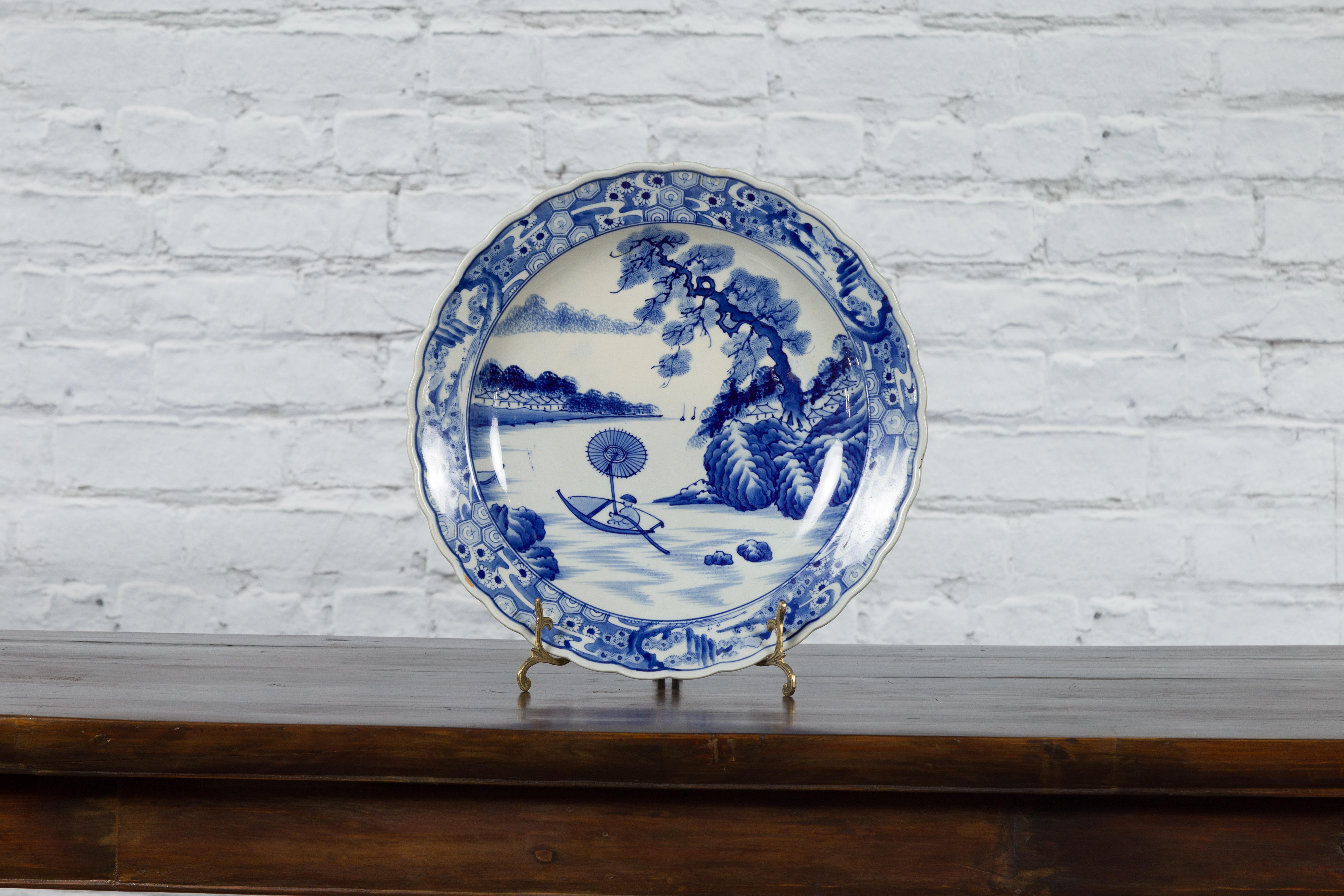 A Japanese Imari porcelain charger plate from the 19th century, with hand-painted blue and white décor depicting a man rowing a boat. Created in Japan during the 19th century, this Imari porcelain charger plate features a delicate blue and white