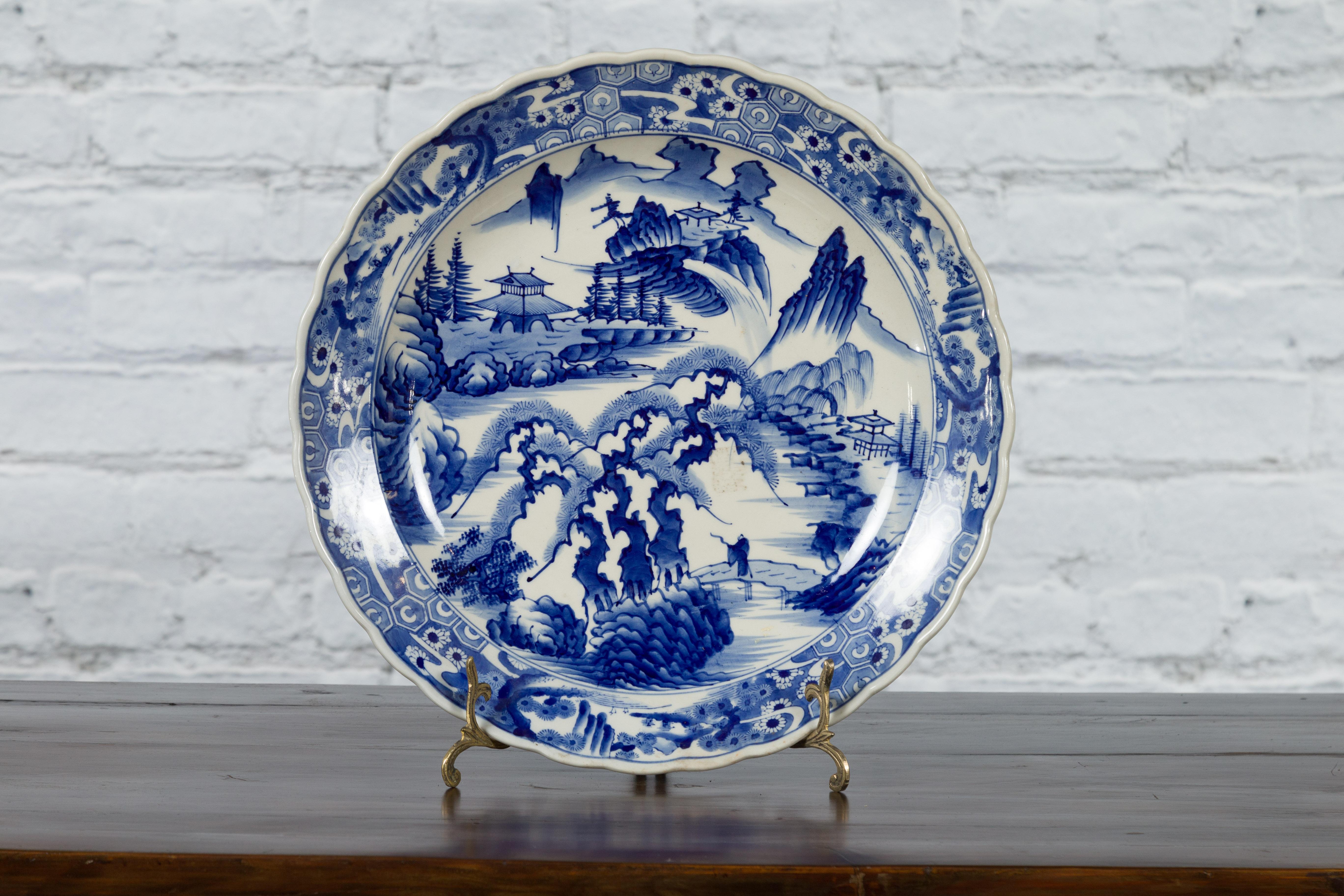 A Japanese Imari porcelain plate from the 19th century, with hand-painted blue and white mountain, tree, architecture and bridge décor. Created in Japan during the 19th century, this Imari porcelain plate features a delicate blue and white décor