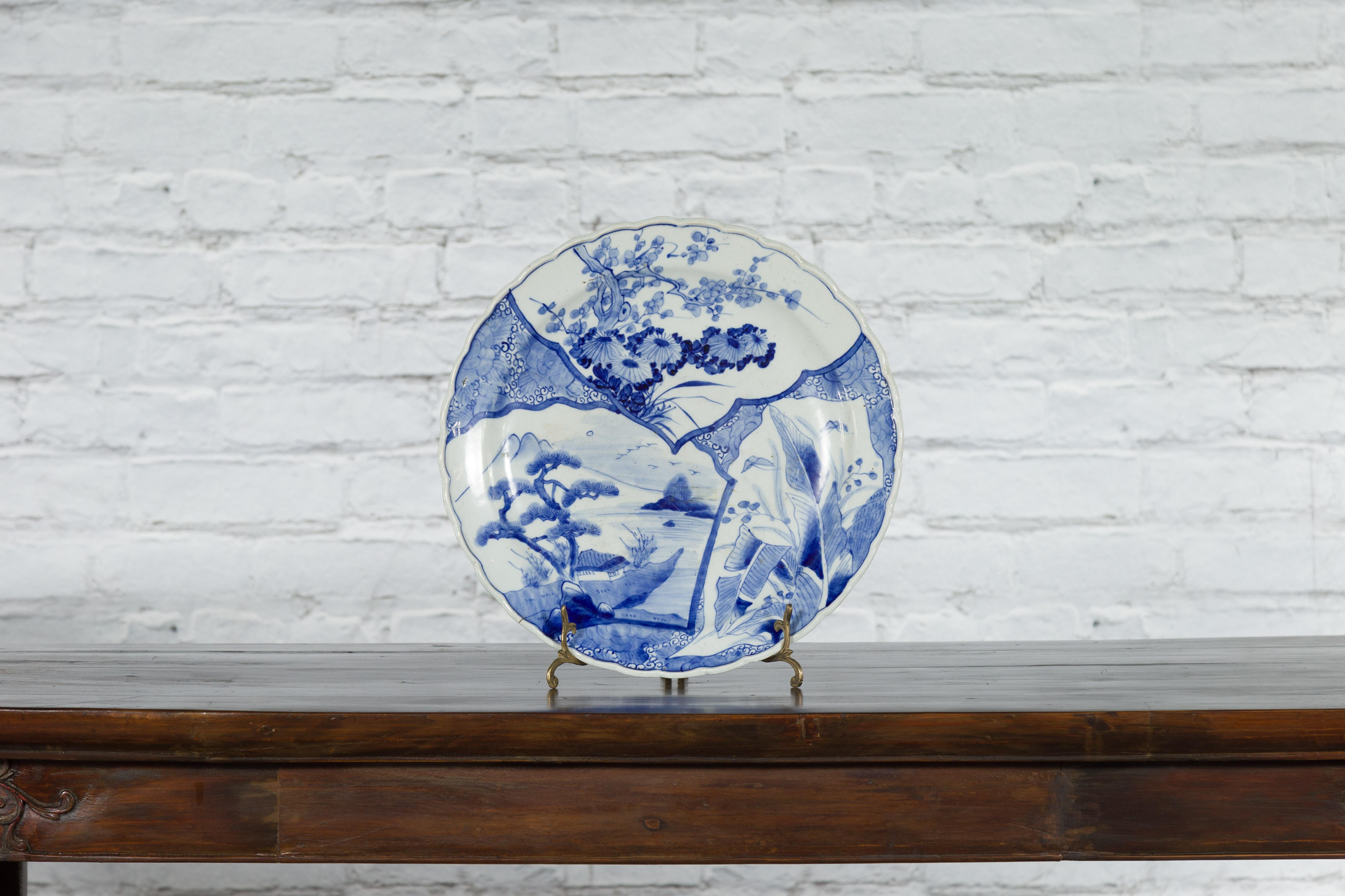 A Japanese Imari porcelain plate from the 19th century, with hand-painted blue and white foliage, tree and architecture décor. Created in Japan during the 19th century, this Imari porcelain plate features a delicate blue and white décor divided into