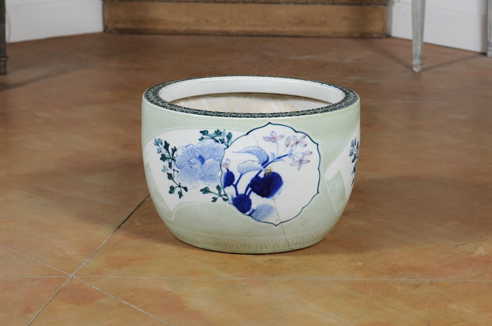 A Japanese goldfish bowl from the 19th century, with soft green ground and blue floral decor. Attracting our attention with its soft colors and delicate decor, this Japanese goldfish bowl features a light green ground accented with white scrolls on