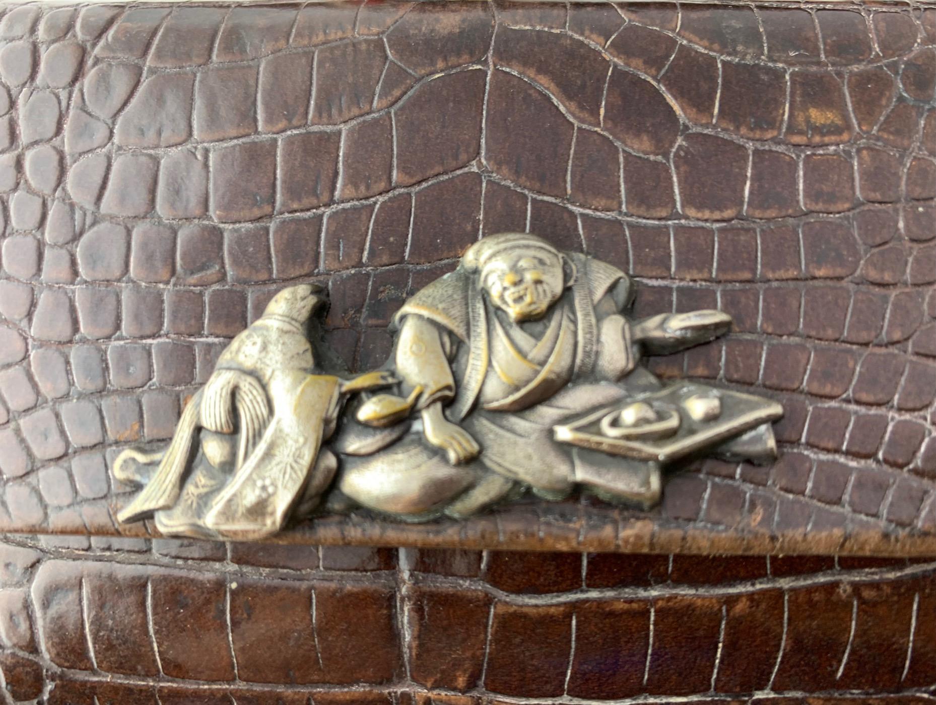 These pieces are a part of smoking set tabako-ire. It consists of a kiseruzutsu (pipe case), a kiseru (pipe), and a tonkotsu (tobacco pouch). The pouch is made of lacquered crocodile leather. Both parts are bound together by a leather link decorated